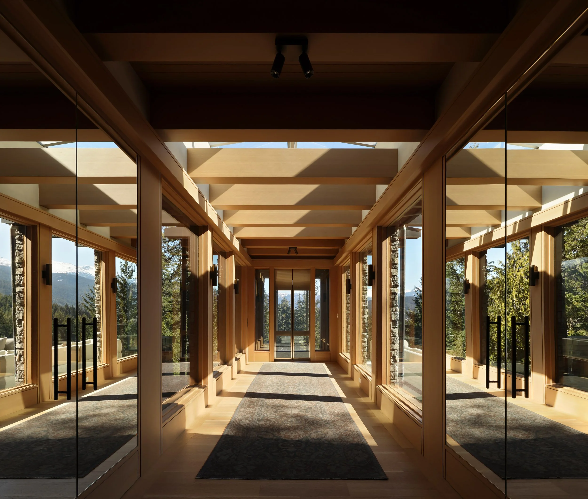 A bright, modern hallway with large glass windows and wooden framing, showcasing scenic mountain views outside.