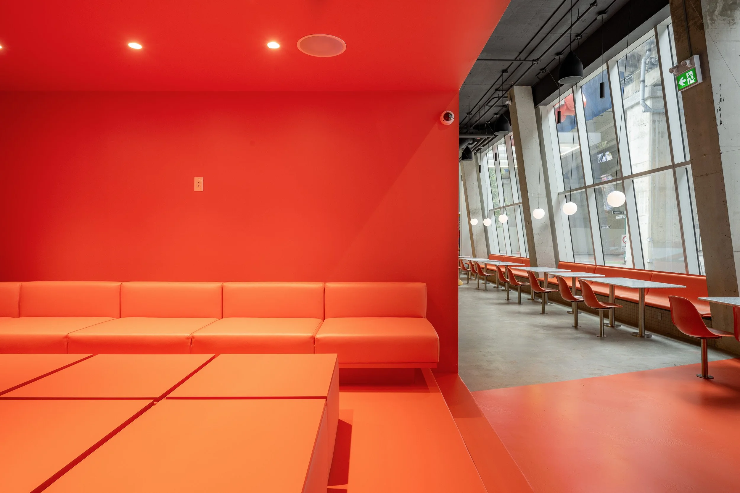 Modern interior of a cafe with a red wall, orange seating, and large windows with angled concrete columns.