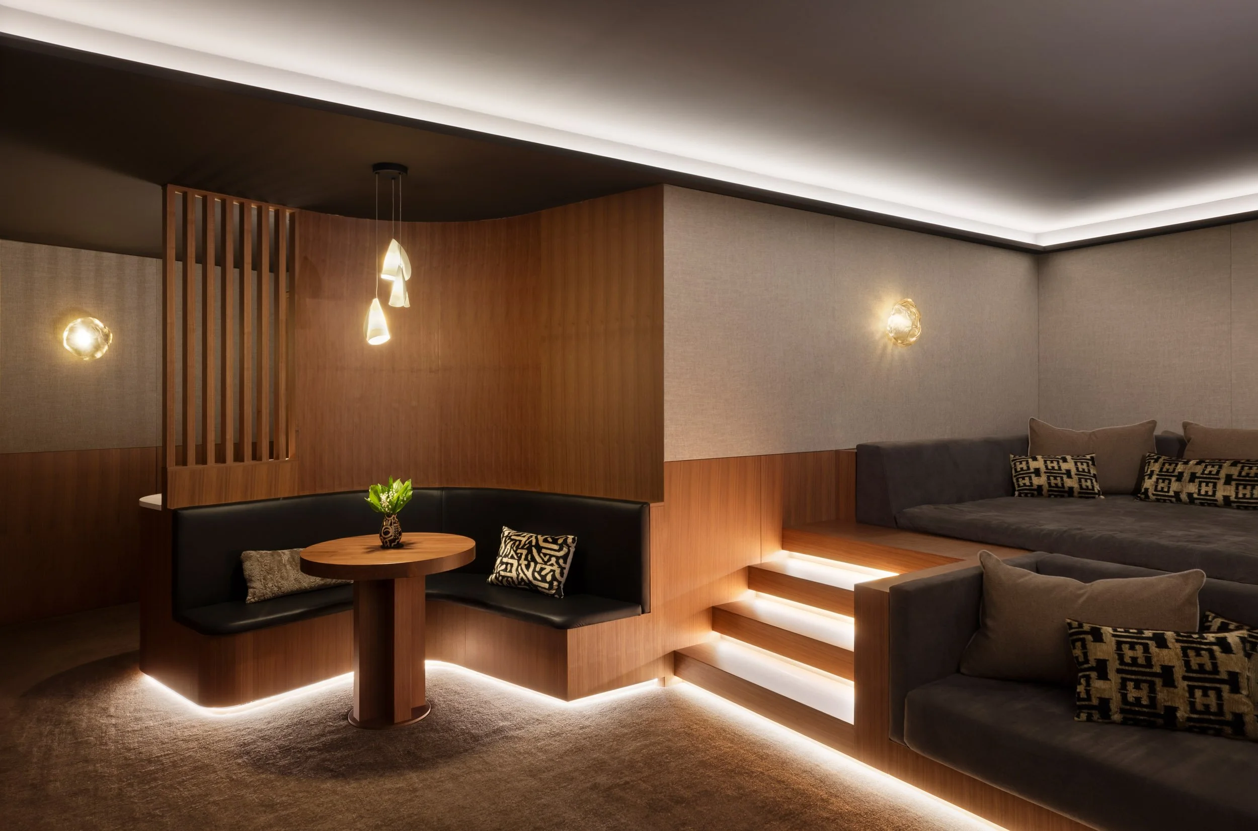 Modern living room with built-in leather seating, wooden accents, recessed lighting, and decorative pillows.
