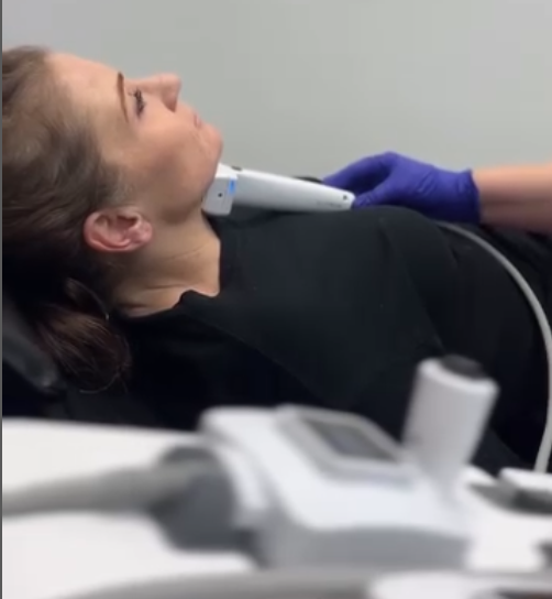 Person receiving a neck ultrasound with a probe, medical equipment in foreground.