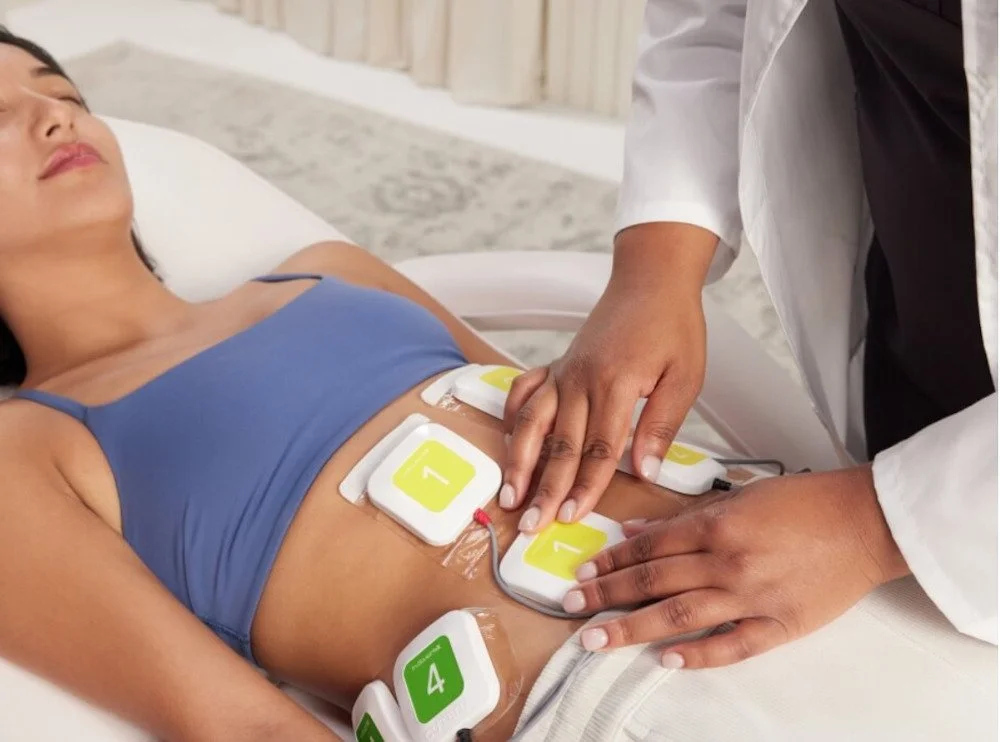 A woman receiving an electrocardiogram on her abdomen, with electrodes attached to her stomach area while lying on a hospital bed.