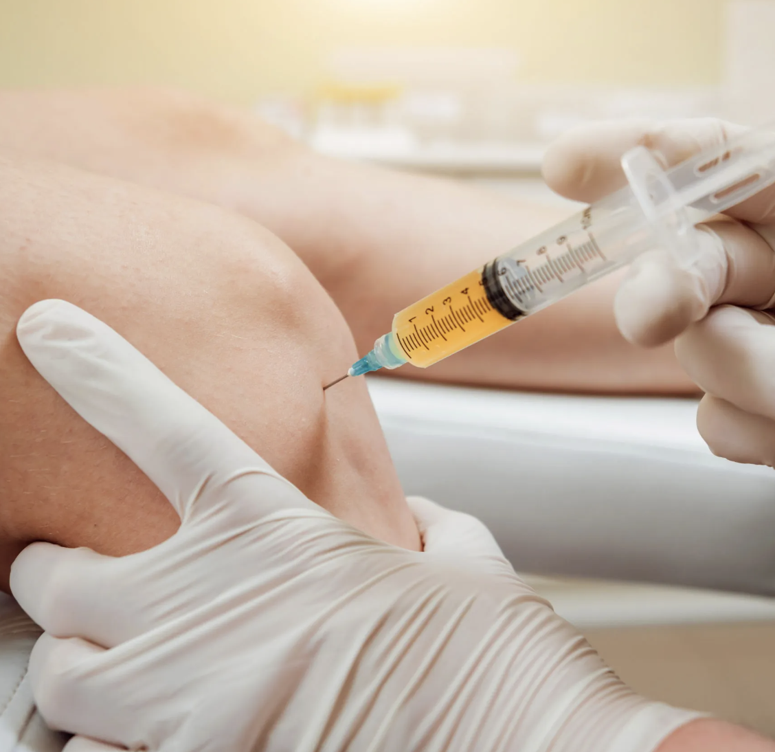 Close-up of a syringe injecting into a person's knee with gloved hands.