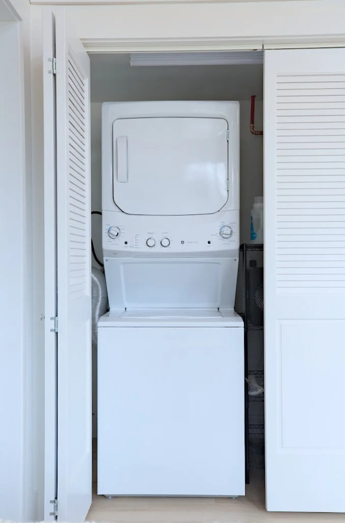 Stacked washer and dryer unit inside a closet with open louvered doors