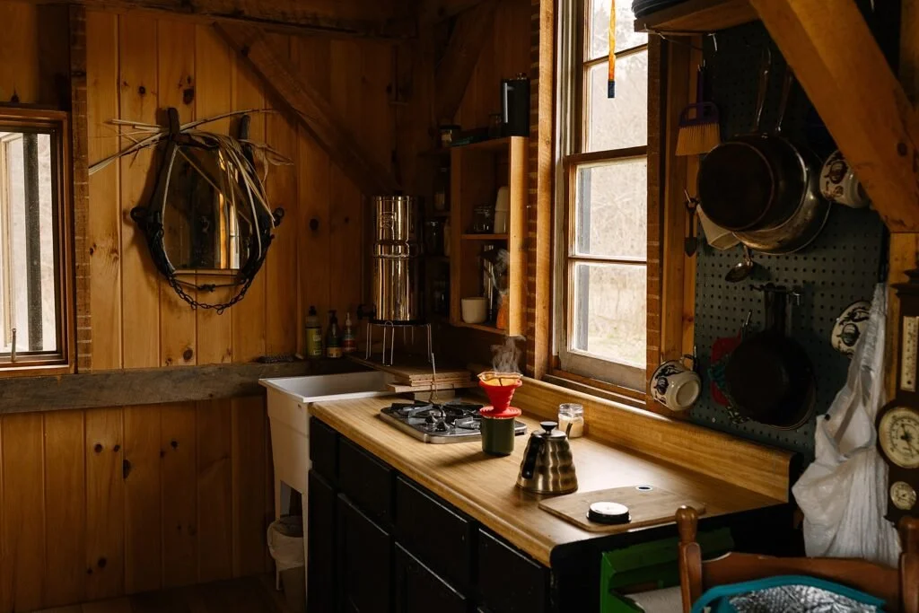 Rustic wooden kitchen with wall-mounted cookware, a countertop coffee setup, window, and a decorative mirror.
