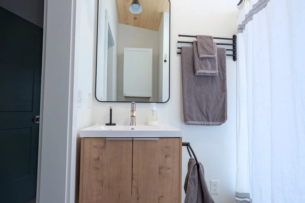 Modern bathroom with wooden vanity, mirror, towels on rack, and shower curtain.