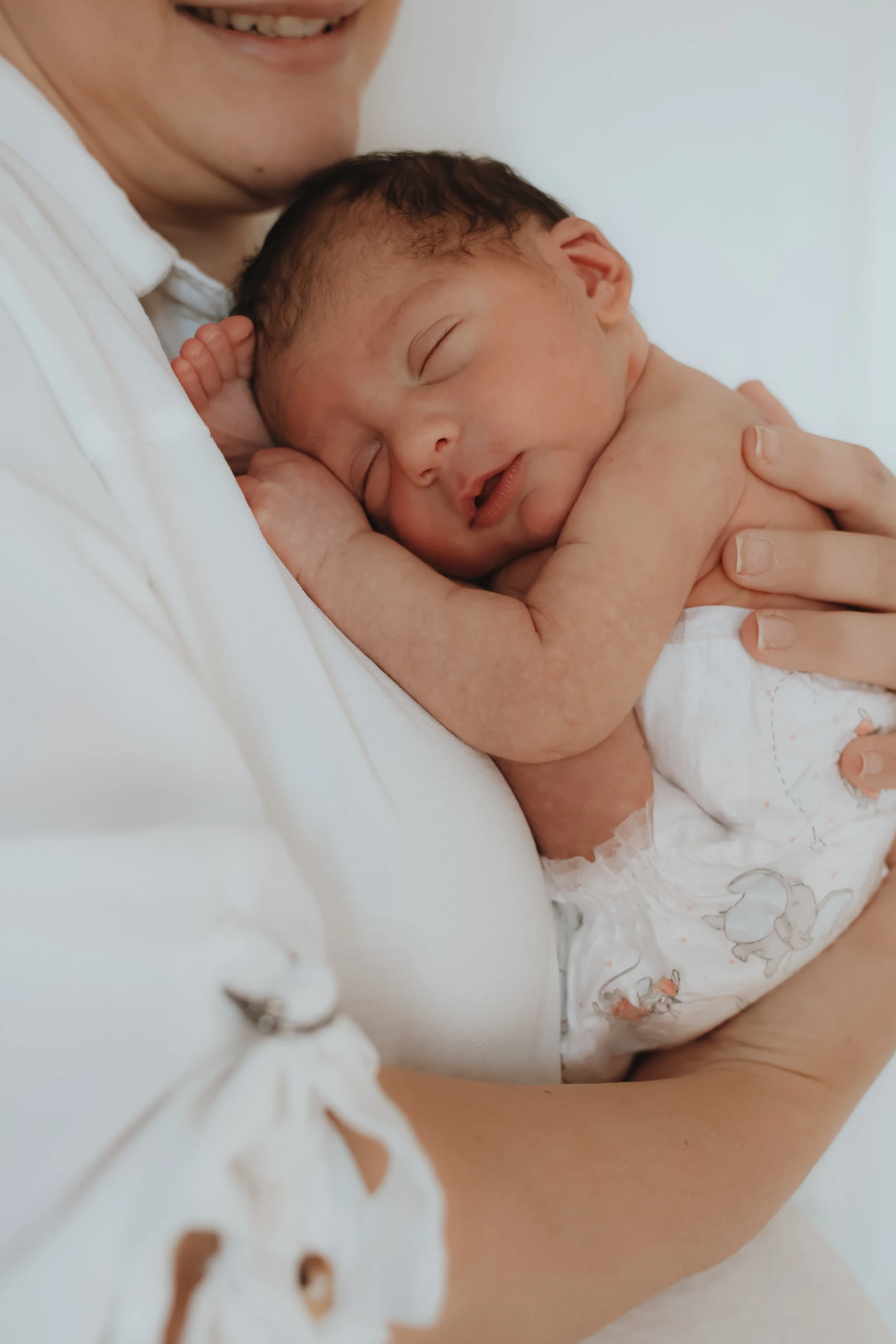 A person holding a sleeping baby newborn to their chest, showing only part of their face and arm, with the baby peacefully resting with eyes closed. In southampton