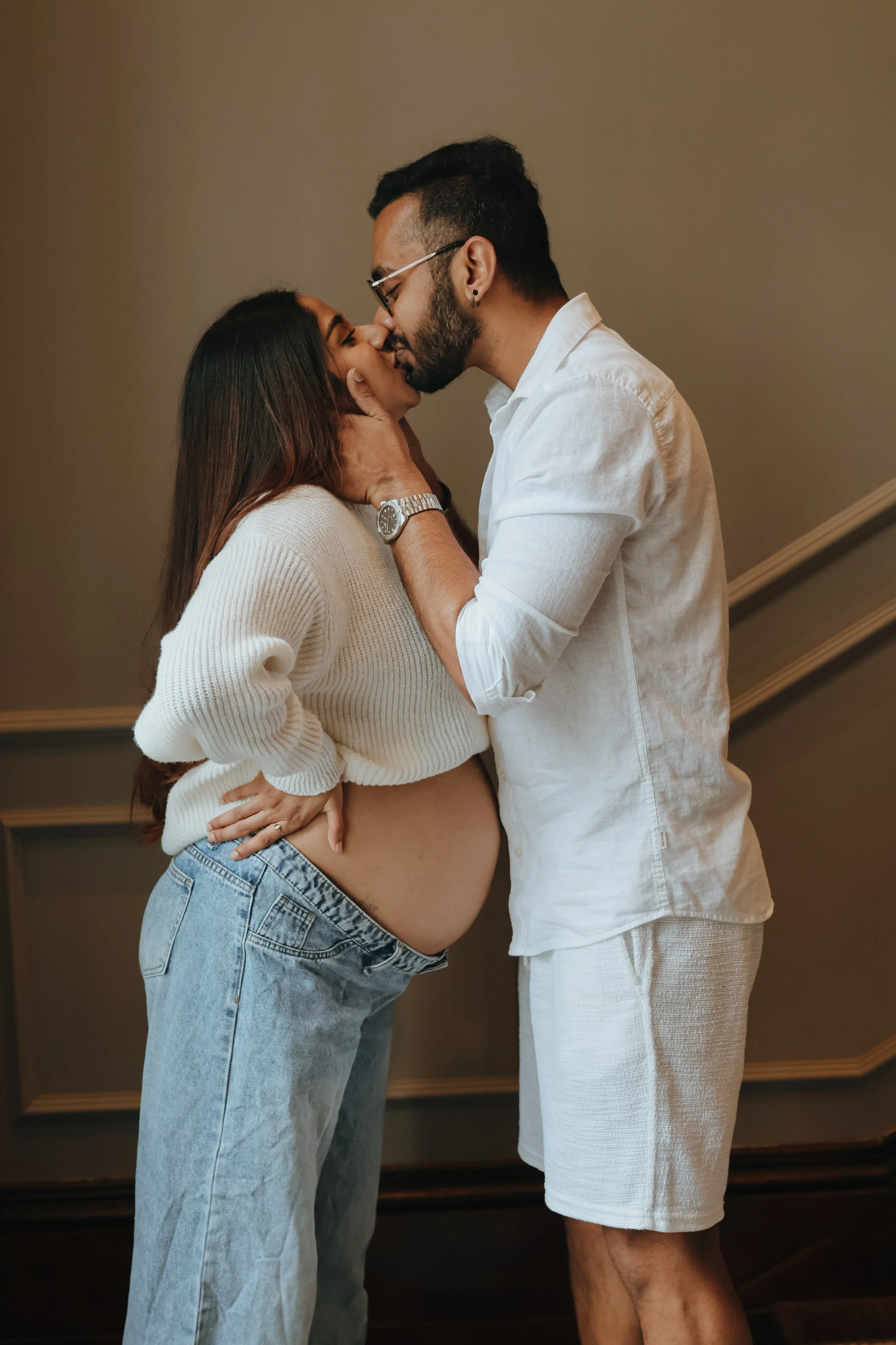 A pregnant woman and a man sharing a kiss indoors, with the man holding the woman's face gently. In hampshire and in southamton, maternity photography