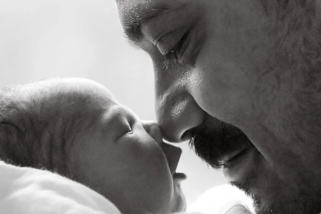 Close-up black and white photograph of a newborn baby and an adult man, likely father, touching their noses together.