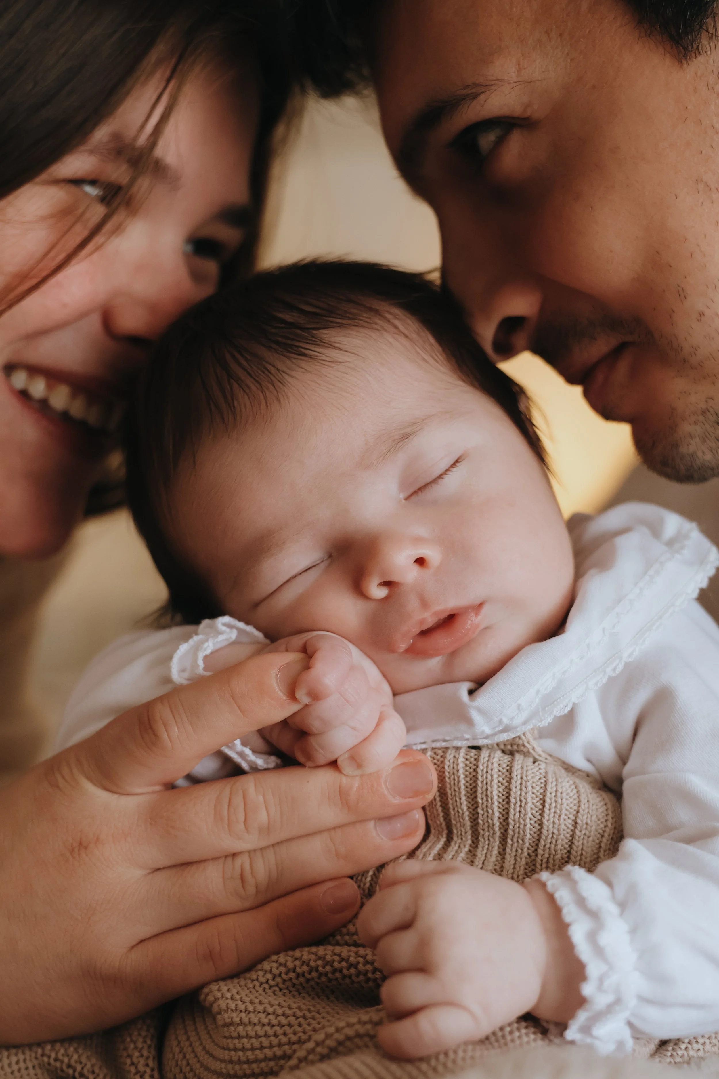 A woman and man gently and lovingly touch foreheads to a sleeping baby's head, with the woman smiling and the man looking at the baby, creating a tender moment. Family, Newborn photography, southampton
