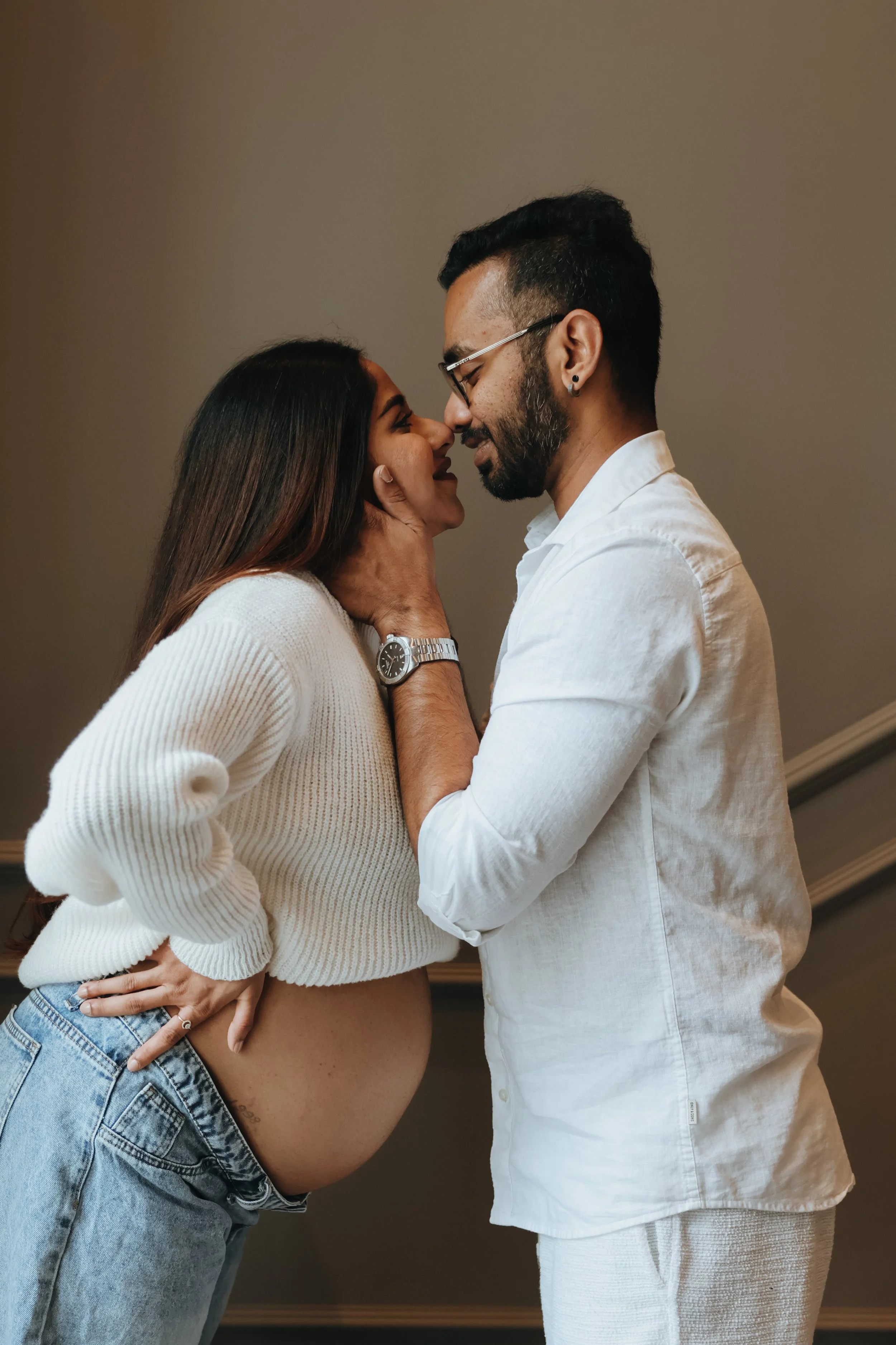 A couple sharing an intimate moment, with the pregnant woman holding her belly and gently touching the man's face, both smiling with eyes closed. Maternity session, maternity photography, Portsmouth 