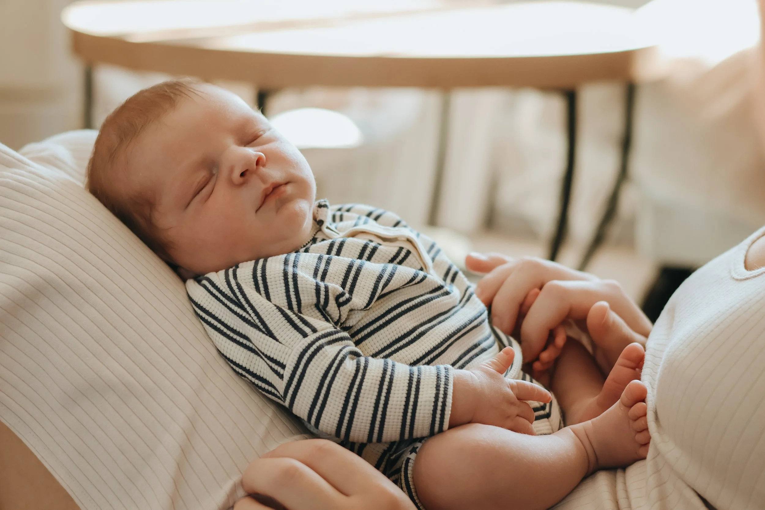 A sleeping baby lying on an adult's chest, holding their hand.