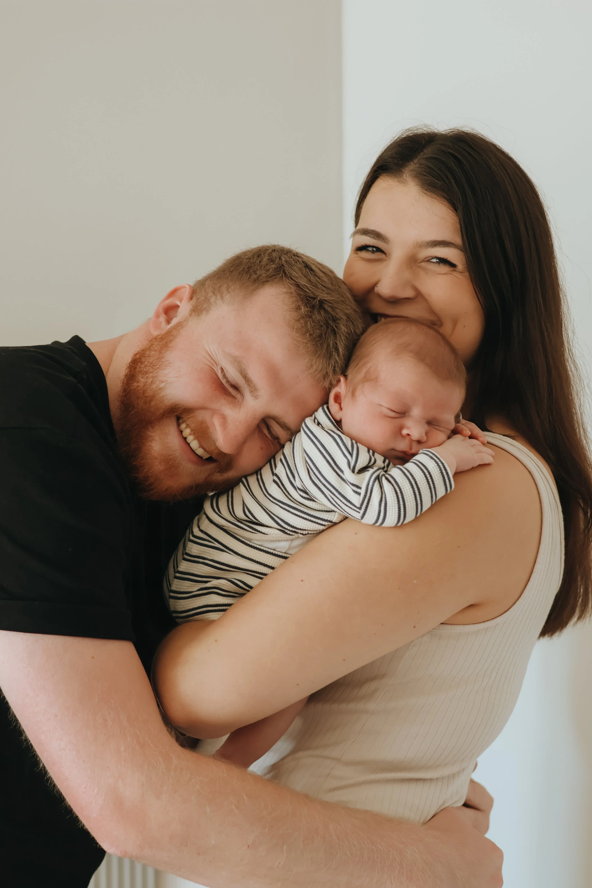 A happy couple holding their sleeping newborn baby close, smiling and embracing each other