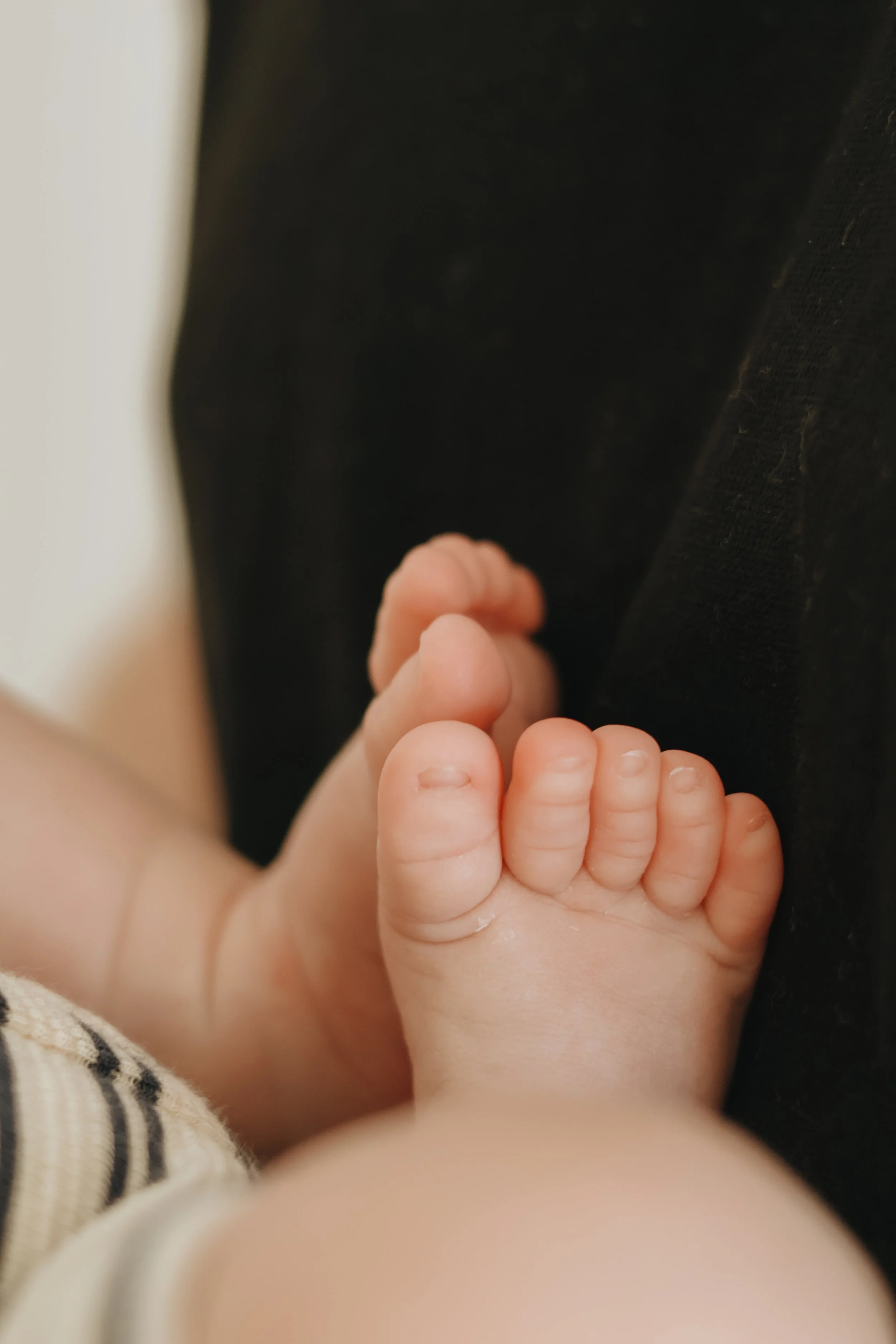 Close-up of a baby's foot resting against a black fabric surface.
