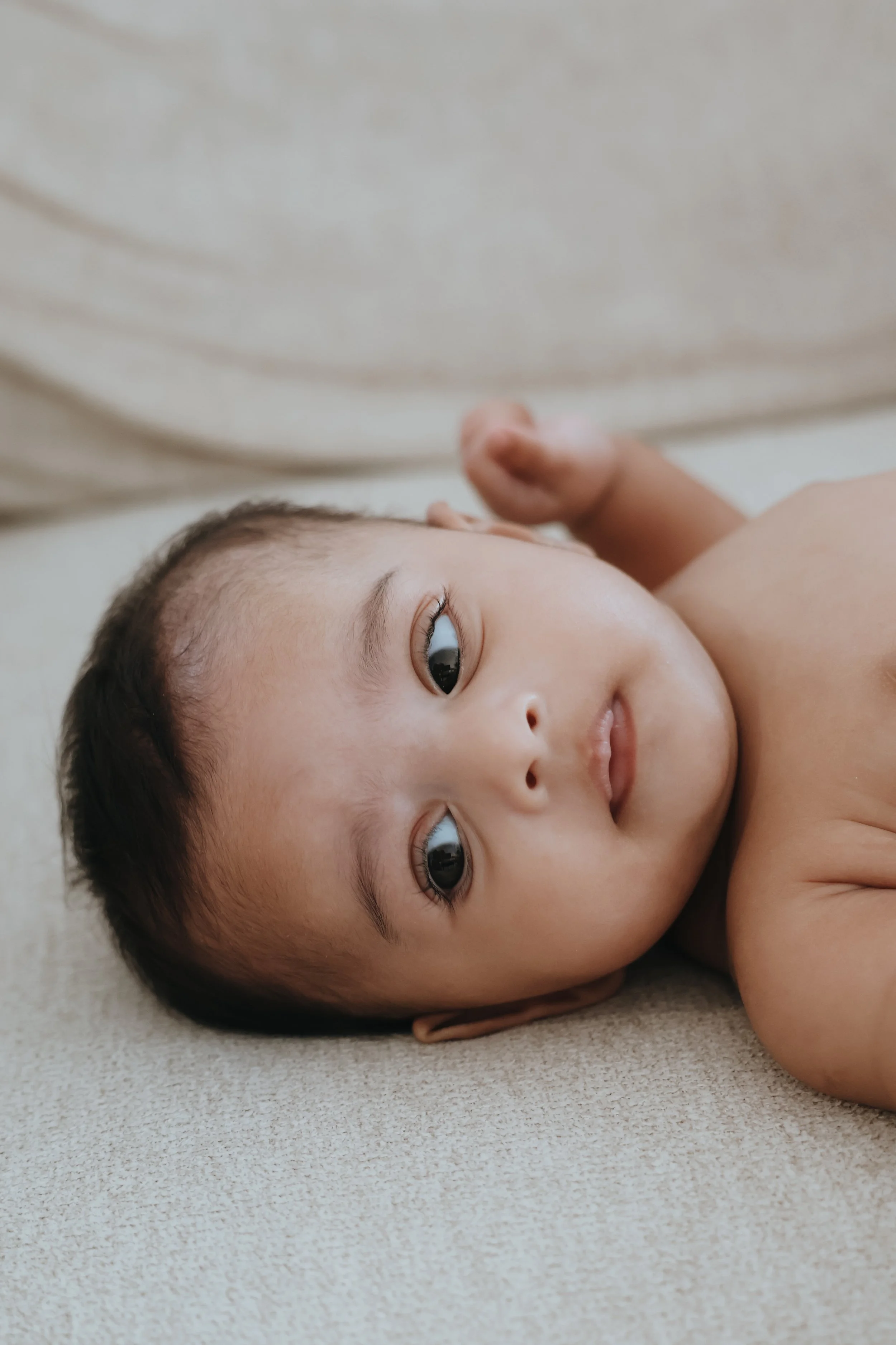 Close-up of a young child lying on a soft surface, looking at the camera with a calm expression.