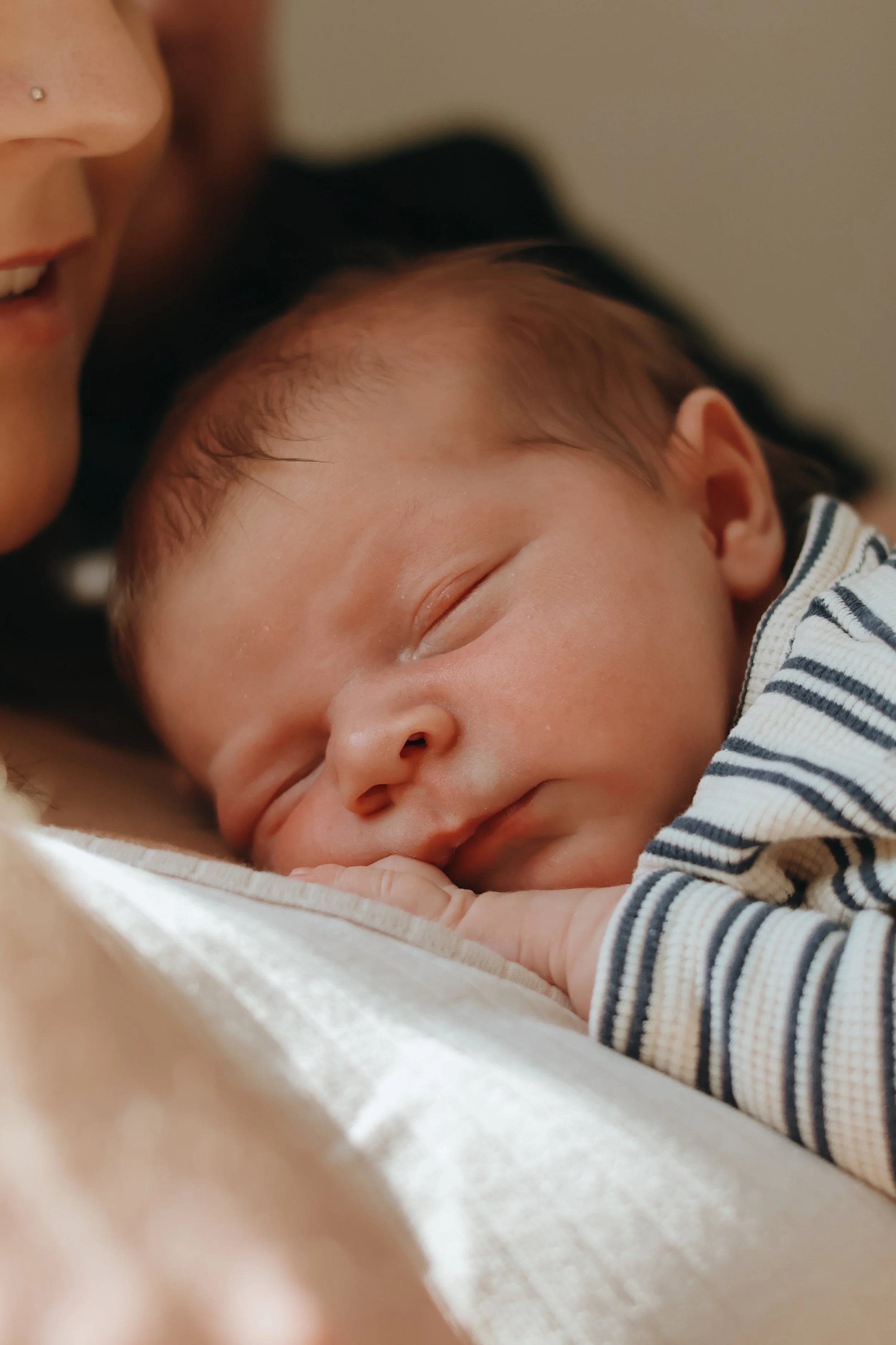 A sleeping baby resting on a person's chest, with details of the person's face partially visible in the frame.