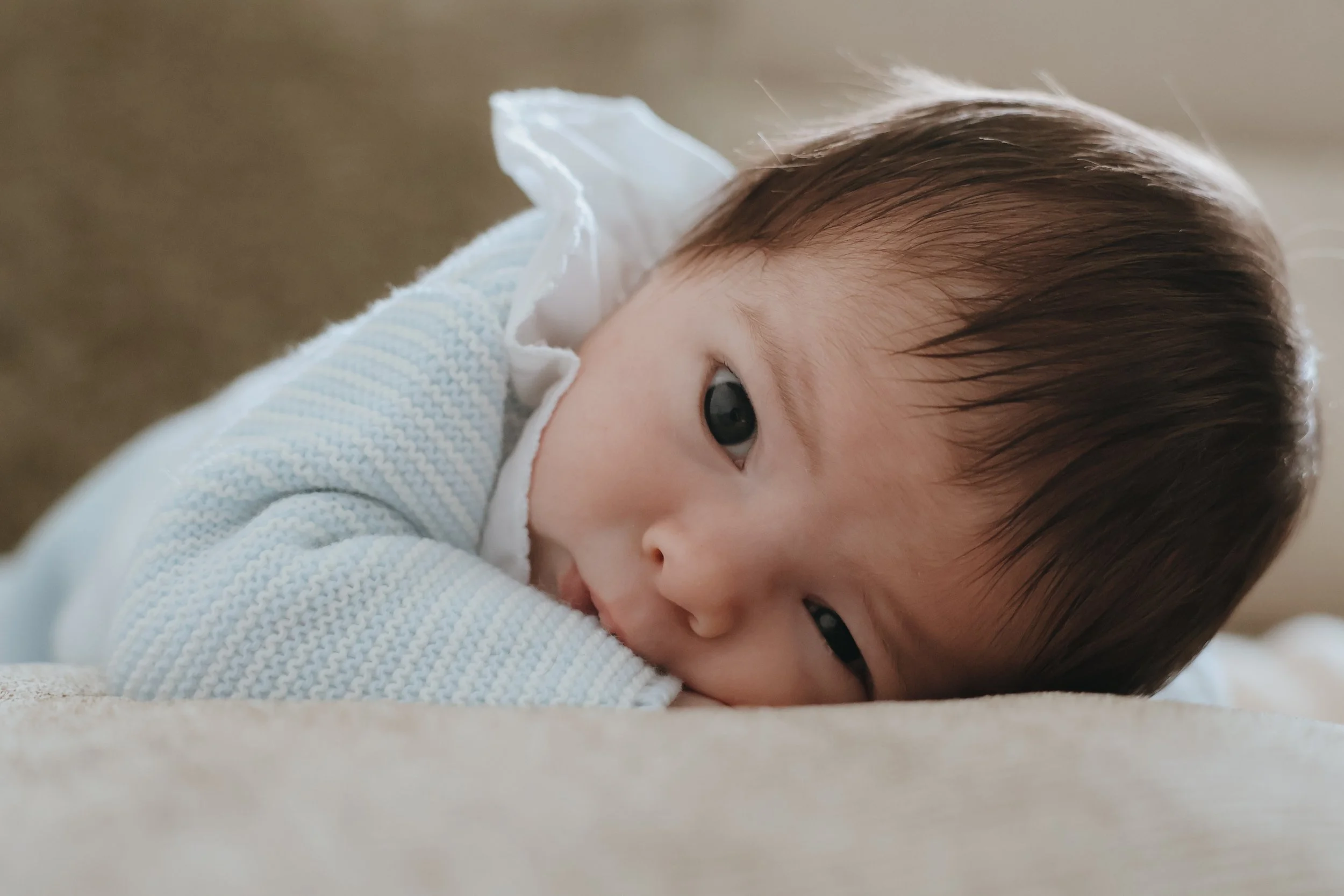 A young child with dark hair lying on a soft surface, resting their head on their arm and looking directly at the camera with a calm expression. Newborn photography, Portsmouth 