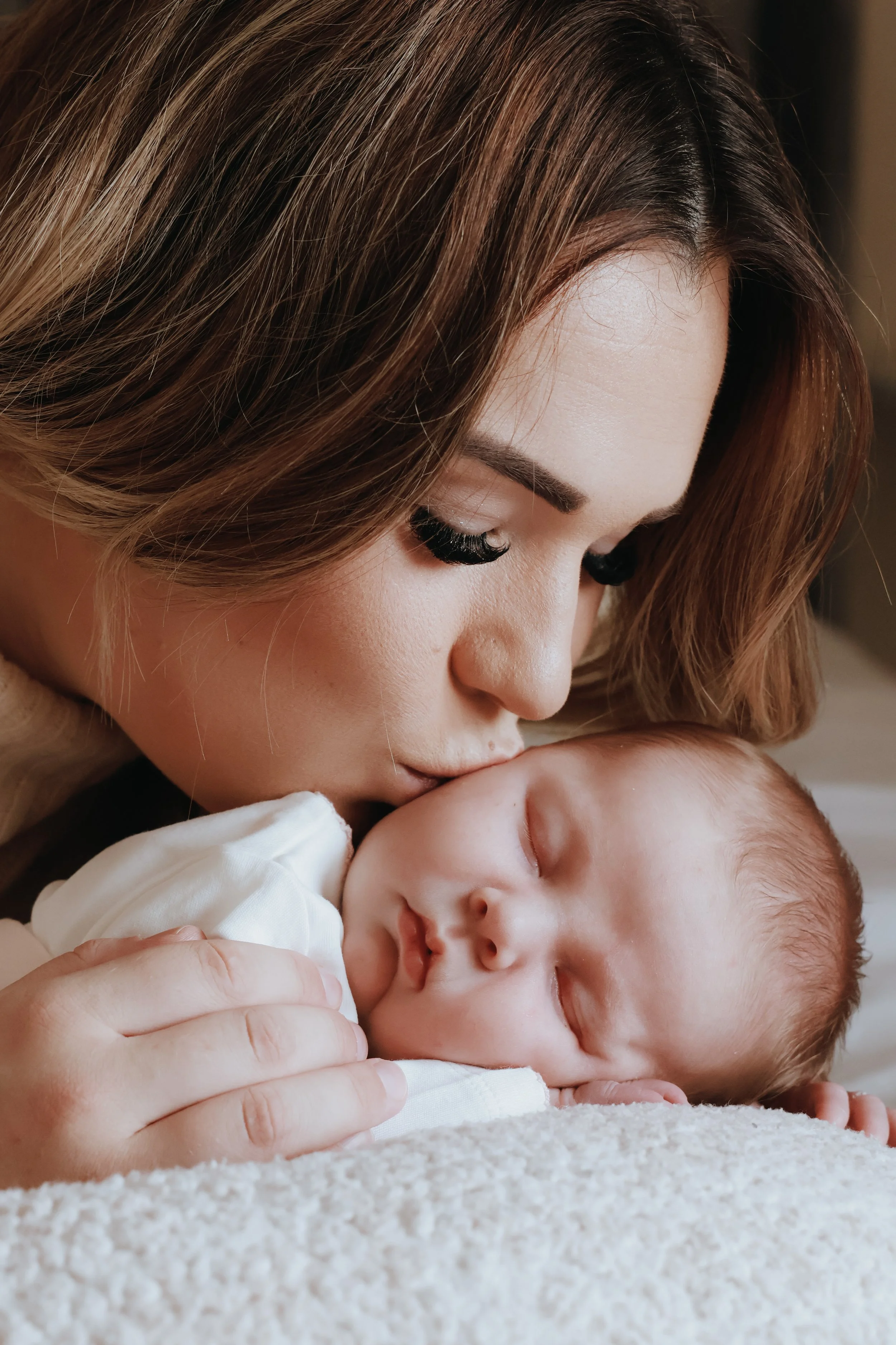 A woman with brown hair kissing a sleeping baby on the forehead. Newborn photography, Portsmouth