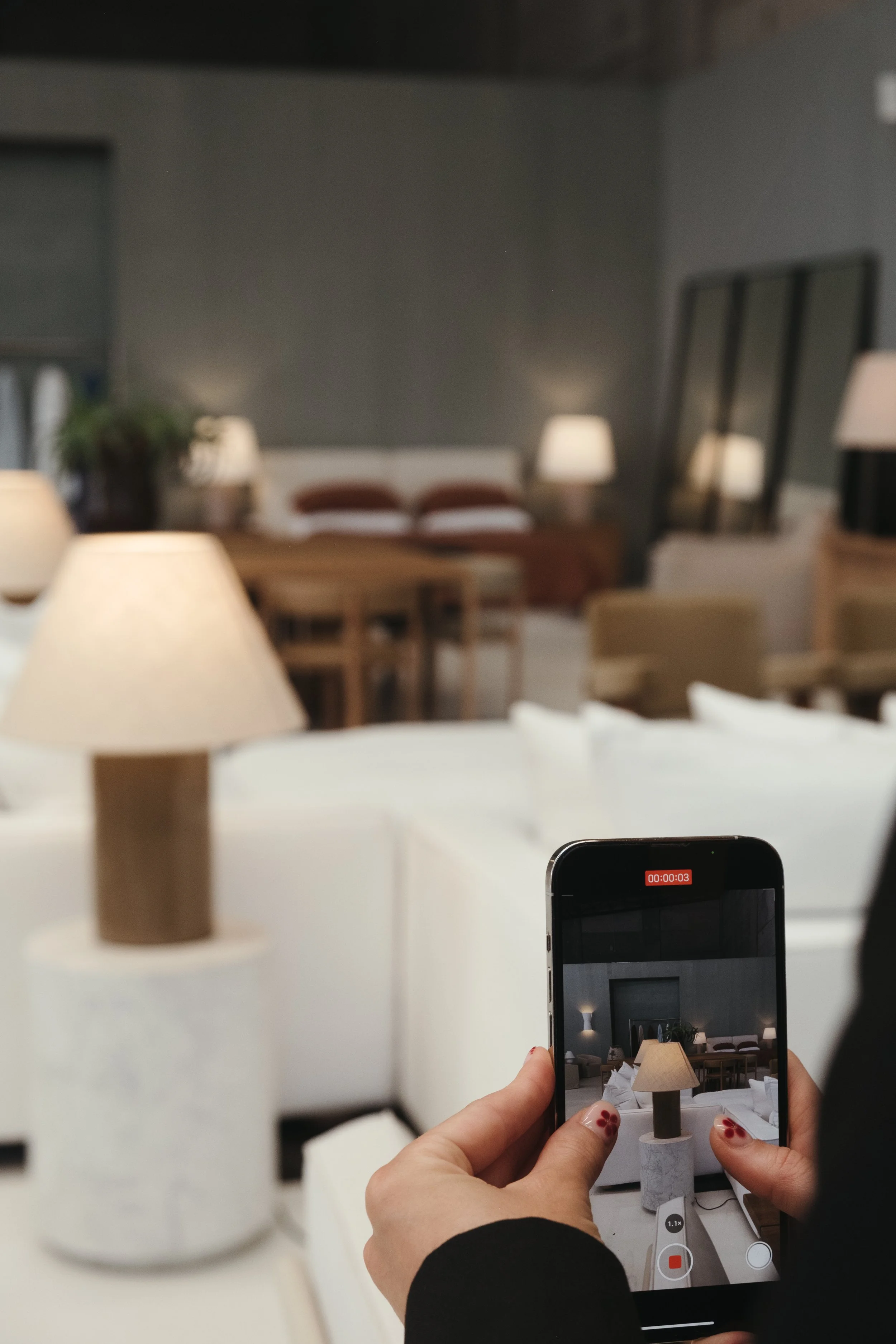 Person recording a video of a table lamp with a smartphone in a living room setting.