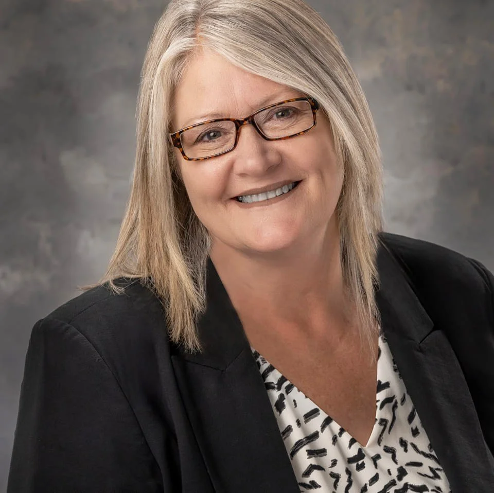 Smiling woman with glasses in a professional portrait, wearing a blazer.