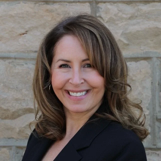 Smiling person in a black suit in front of a stone wall
