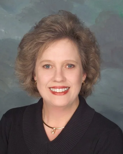 Smiling person with short blonde hair in front of brick wall