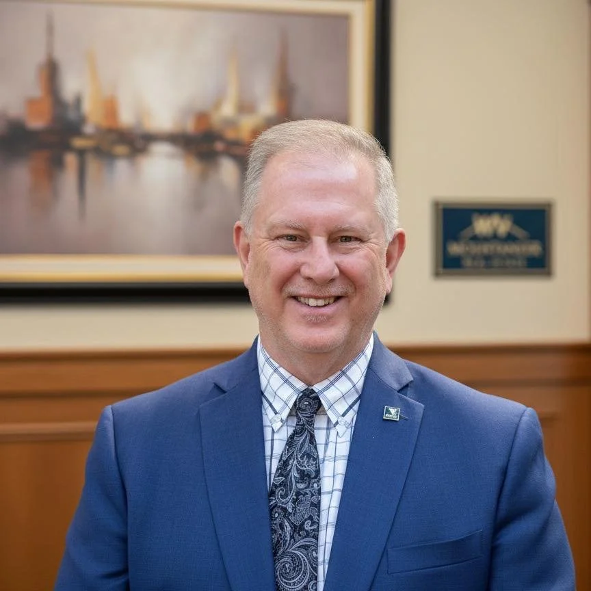 Confident middle-aged man in business attire smiling with arms crossed against a blue background.