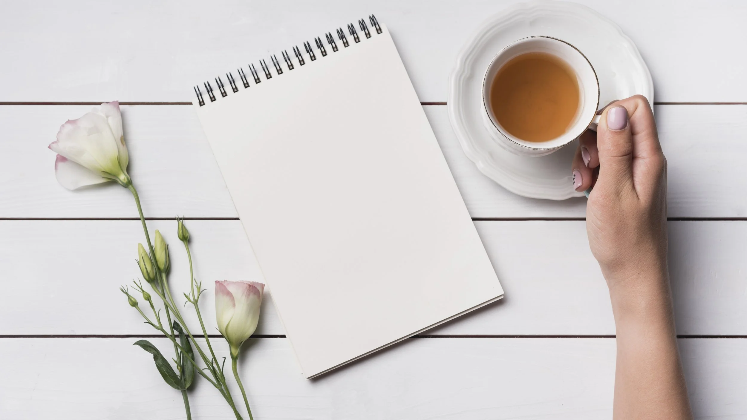Overhead view of person holding a cup of tea and looking over a notepad.