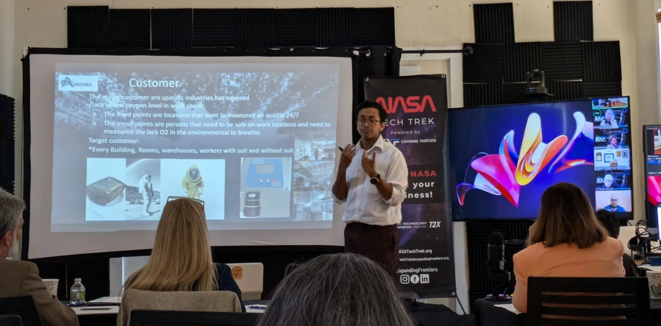 A man giving a presentation at a conference, with a projected slide about customer industries, in front of an audience.