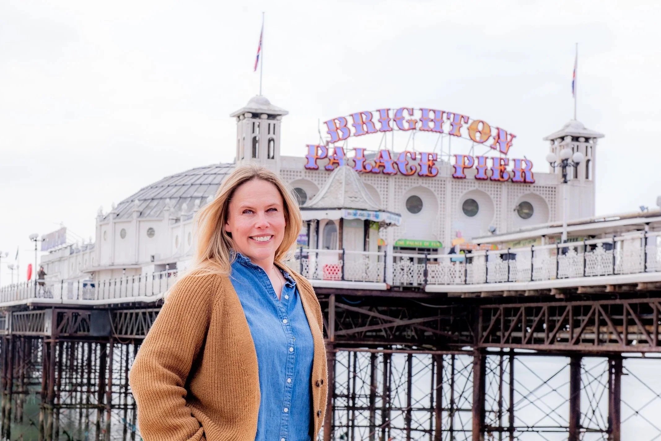 Gayle, Founder Tide & Bloom standing in front of Brighton Palace Pier, wearing brown cardigan and blue denim shirt