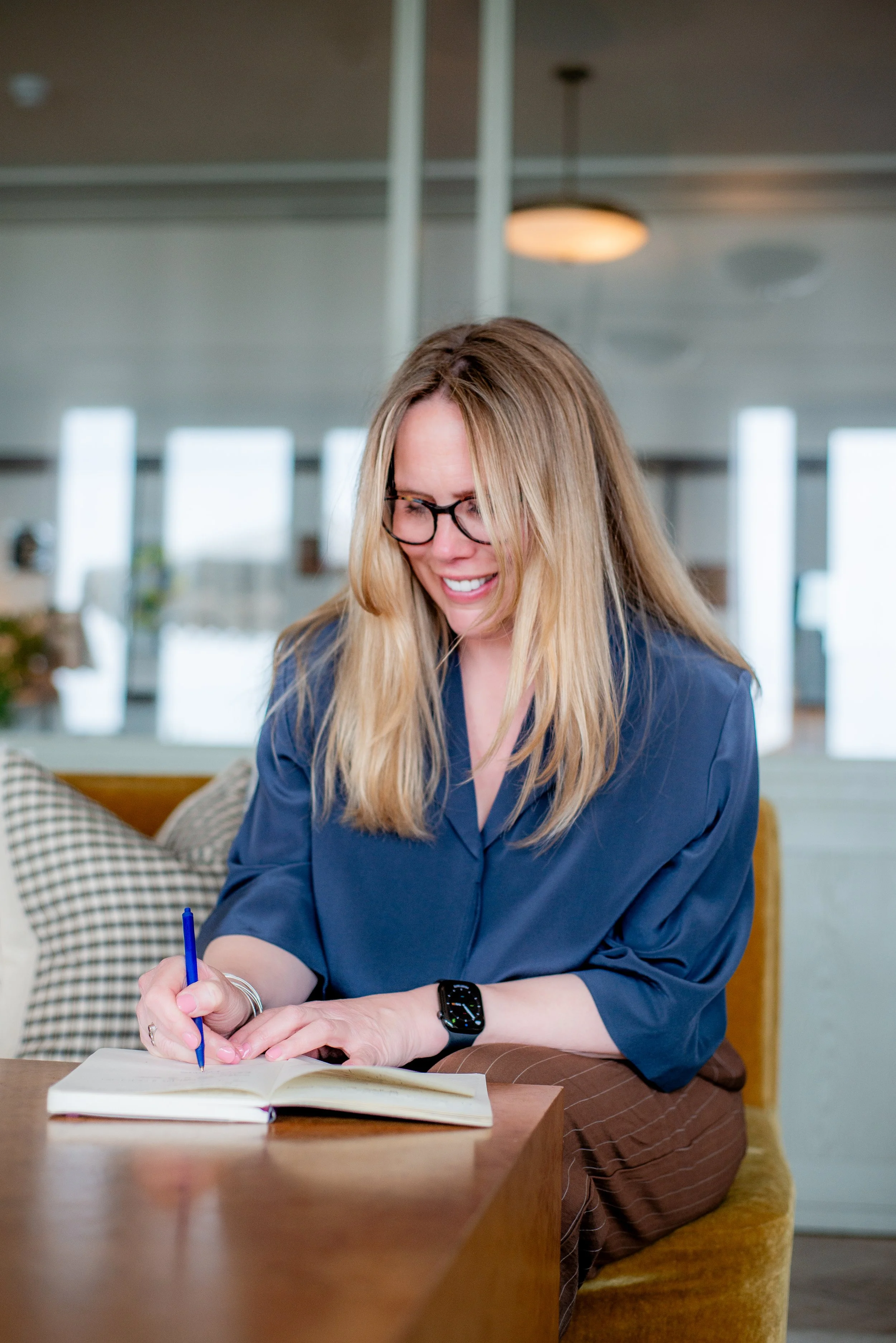 Gayle Jones, Founder or Tide & Bloom wearing blue shirt with blue pen in hand, writing