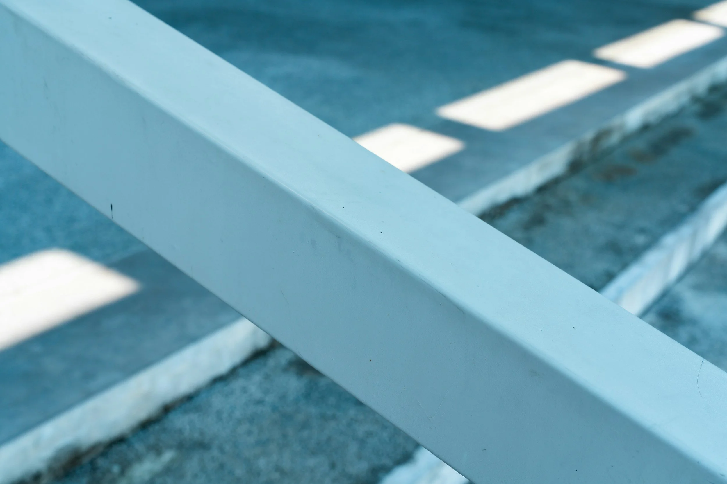 Close-up of white horizontal railing with shadow patterns on an outdoor gray surface.