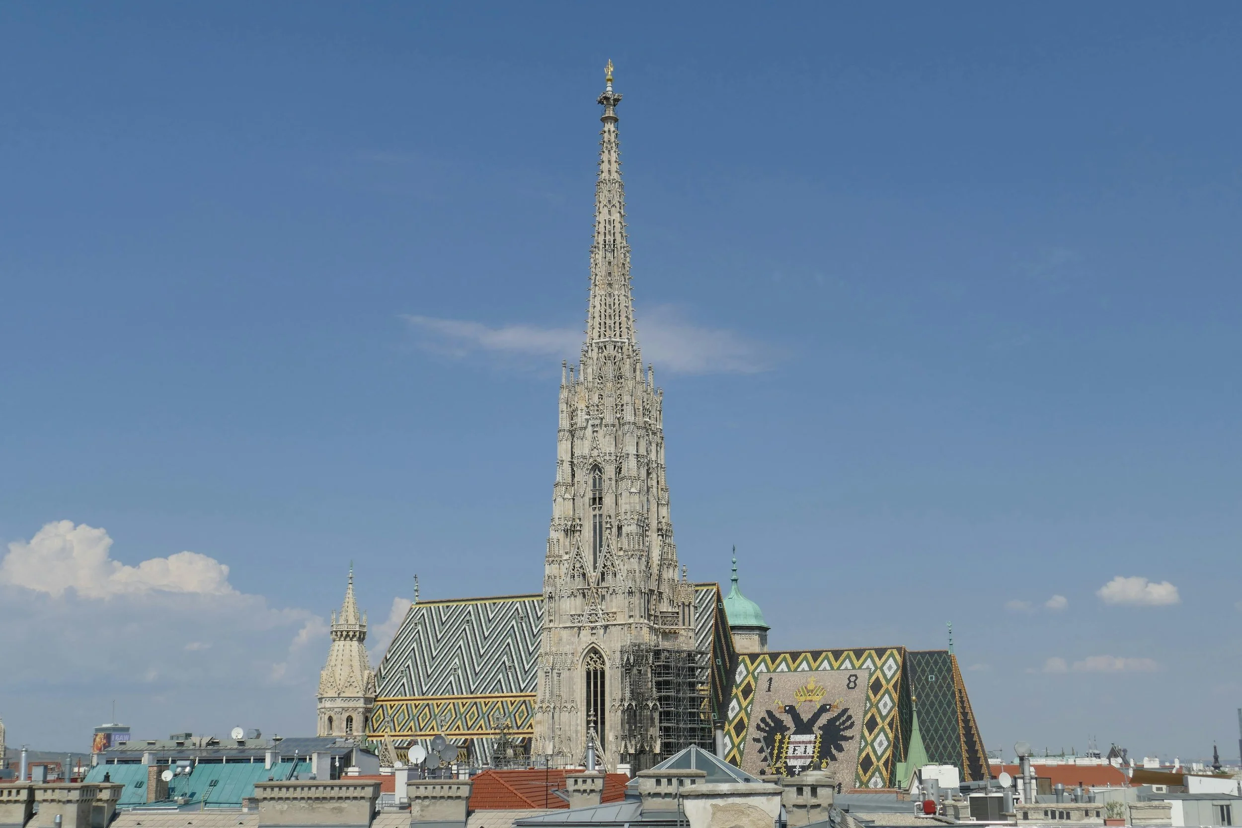 St. Stephen's Cathedral in Vienna, Austria, featuring a tall Gothic spire and a colorful tiled roof with geometric patterns, under a clear blue sky.