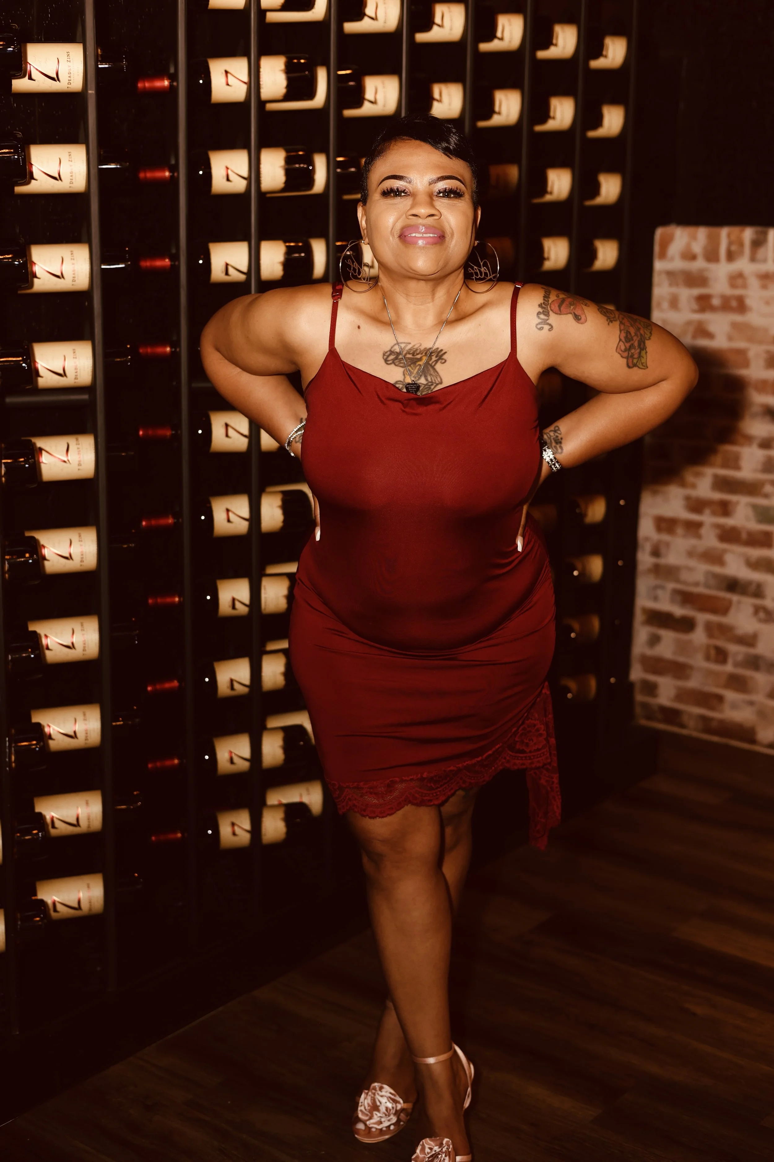 Smiling woman with floral tattoos in a colorful, floral-themed cafe.