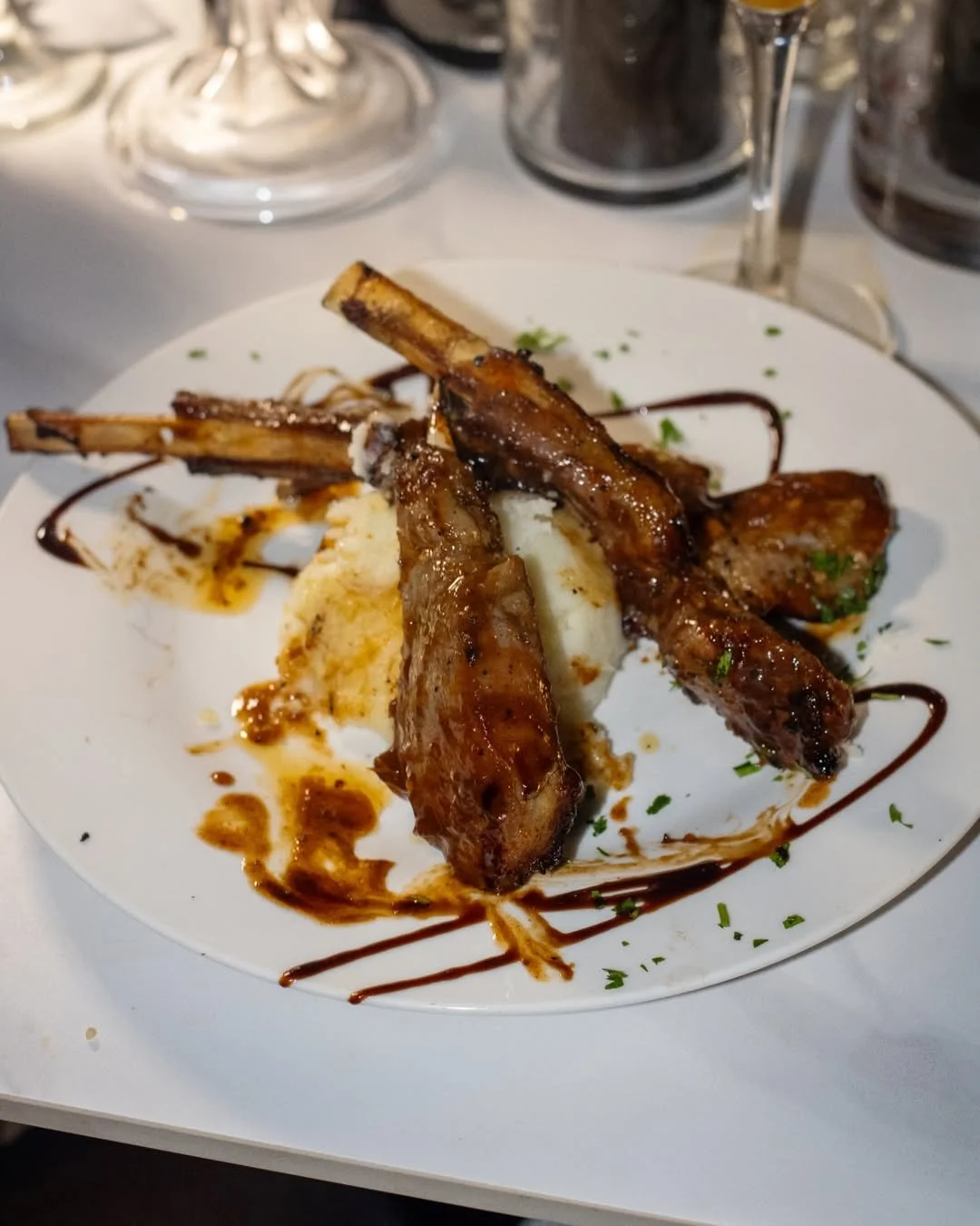 Plate of grilled lamb chops with mashed potatoes, garnished with sauce and herbs.