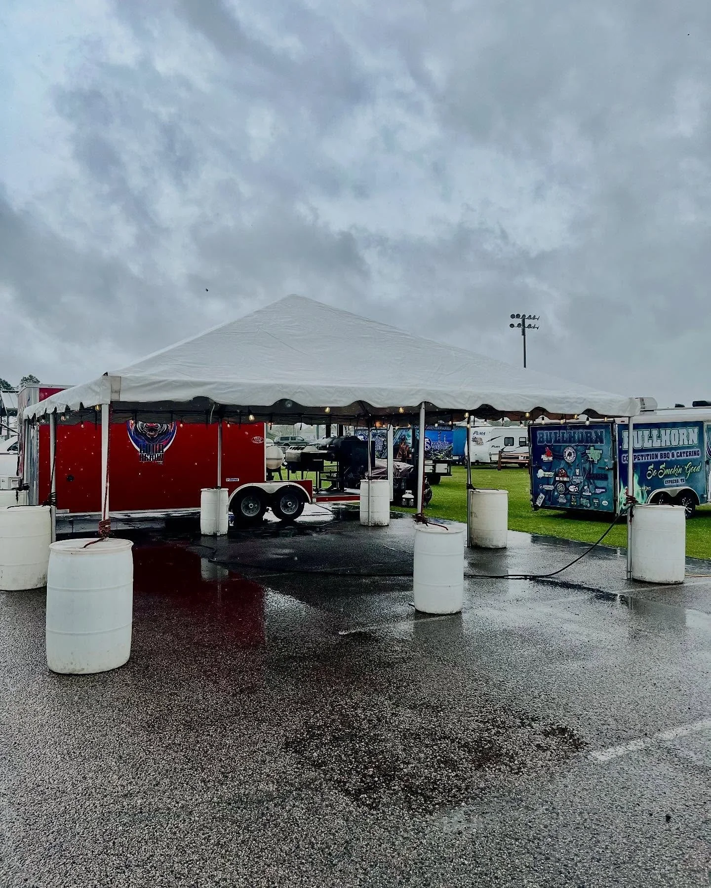 Empty outdoor tent and food trucks on a wet parking lot on a cloudy day.