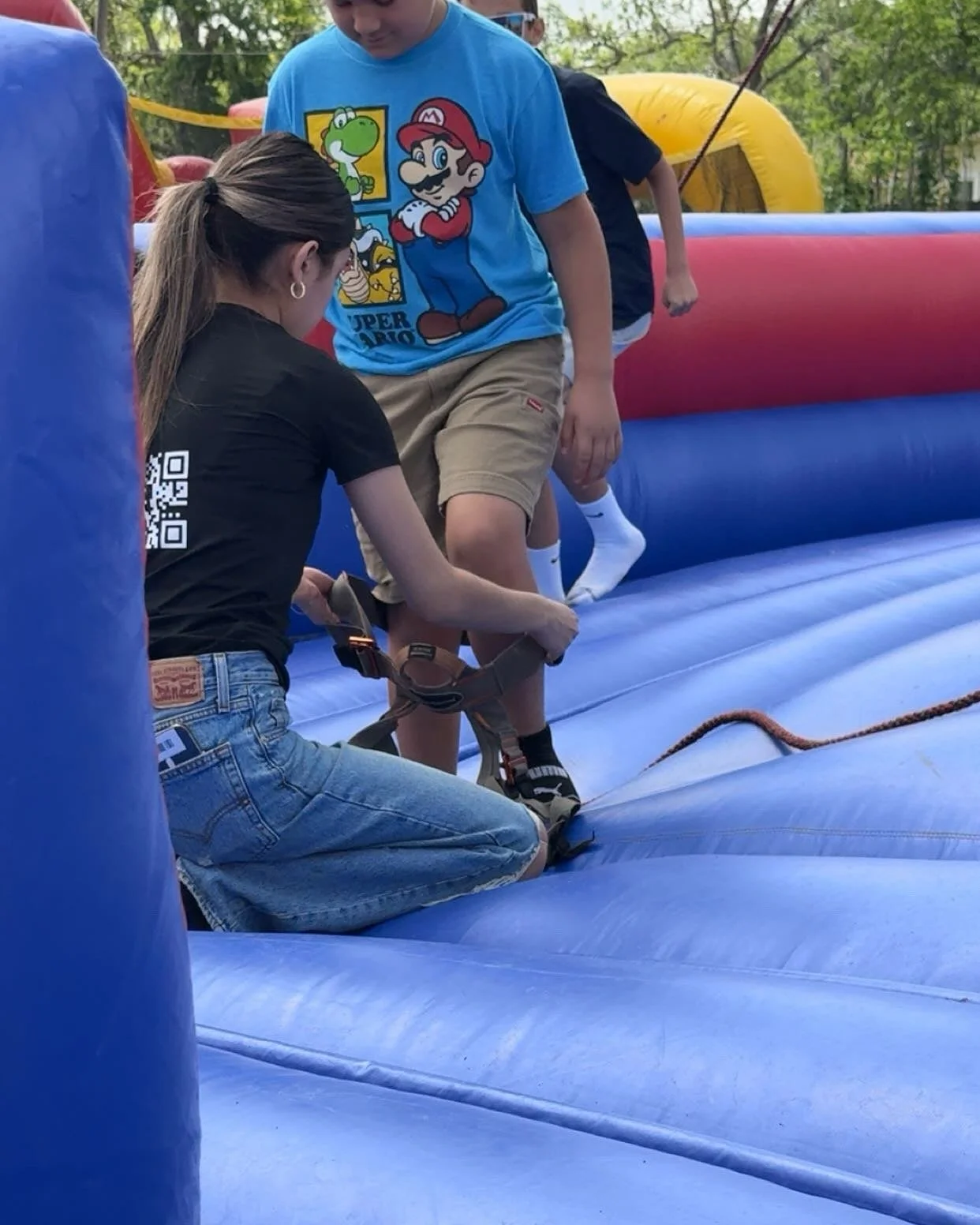 A woman helping children on an inflatable bounce house during an outdoor event.