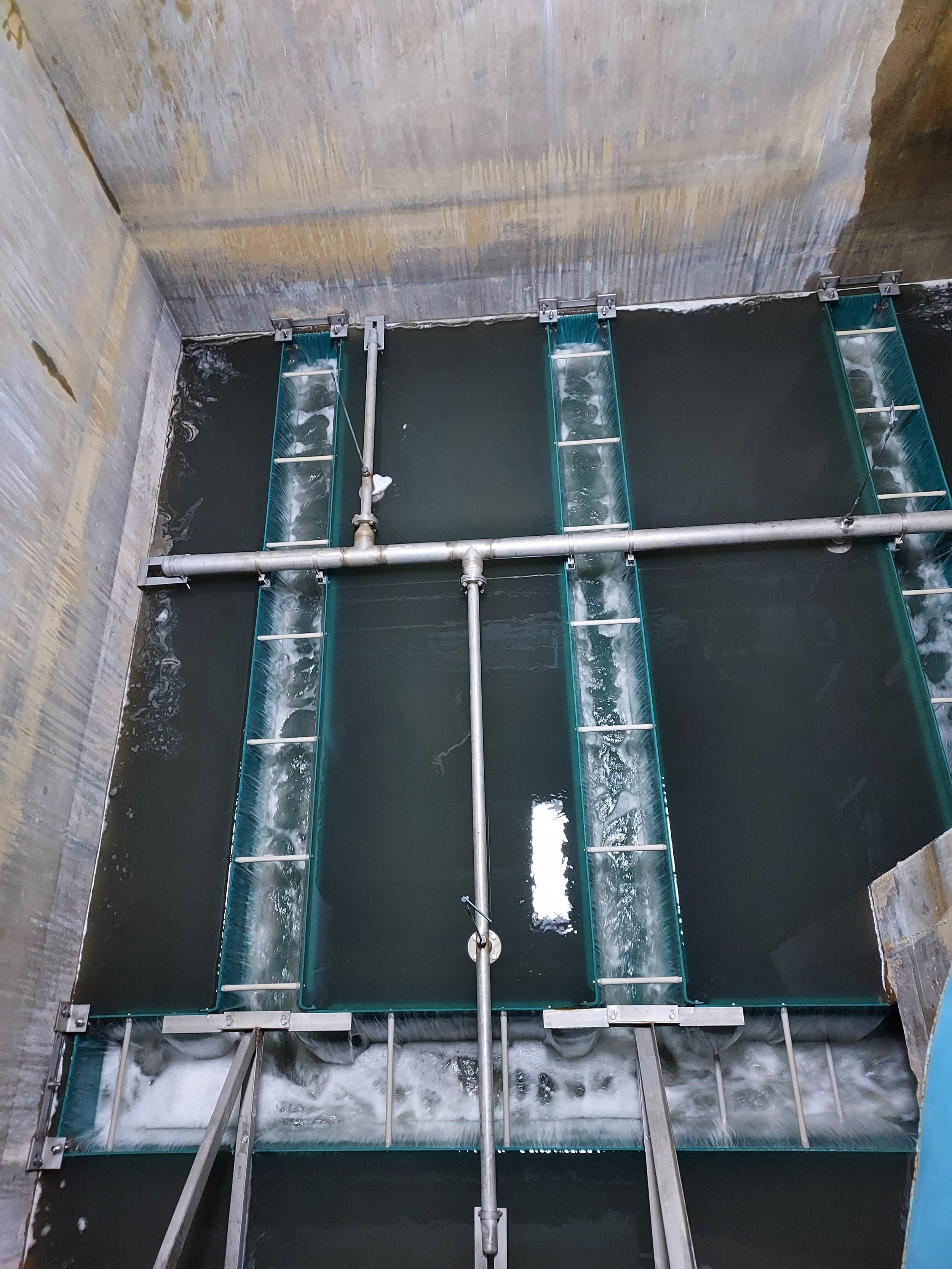 An industrial water filtration system with several mesh screens and pipes in a concrete tank