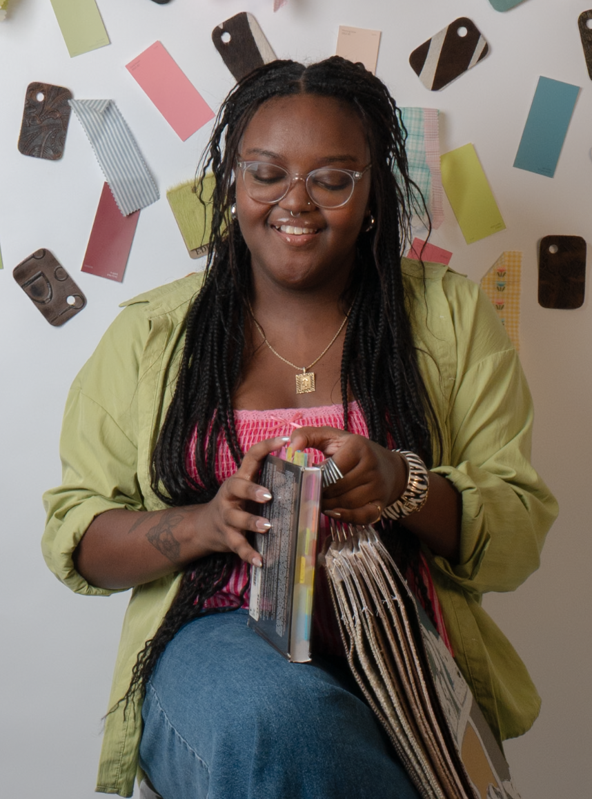 A woman with long braided hair, glasses, and a nose ring, smiling while looking at colorful folders and papers.