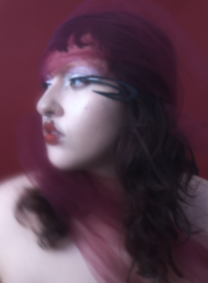Portrait of a woman with purple hair, wearing glasses with a blurred red background.