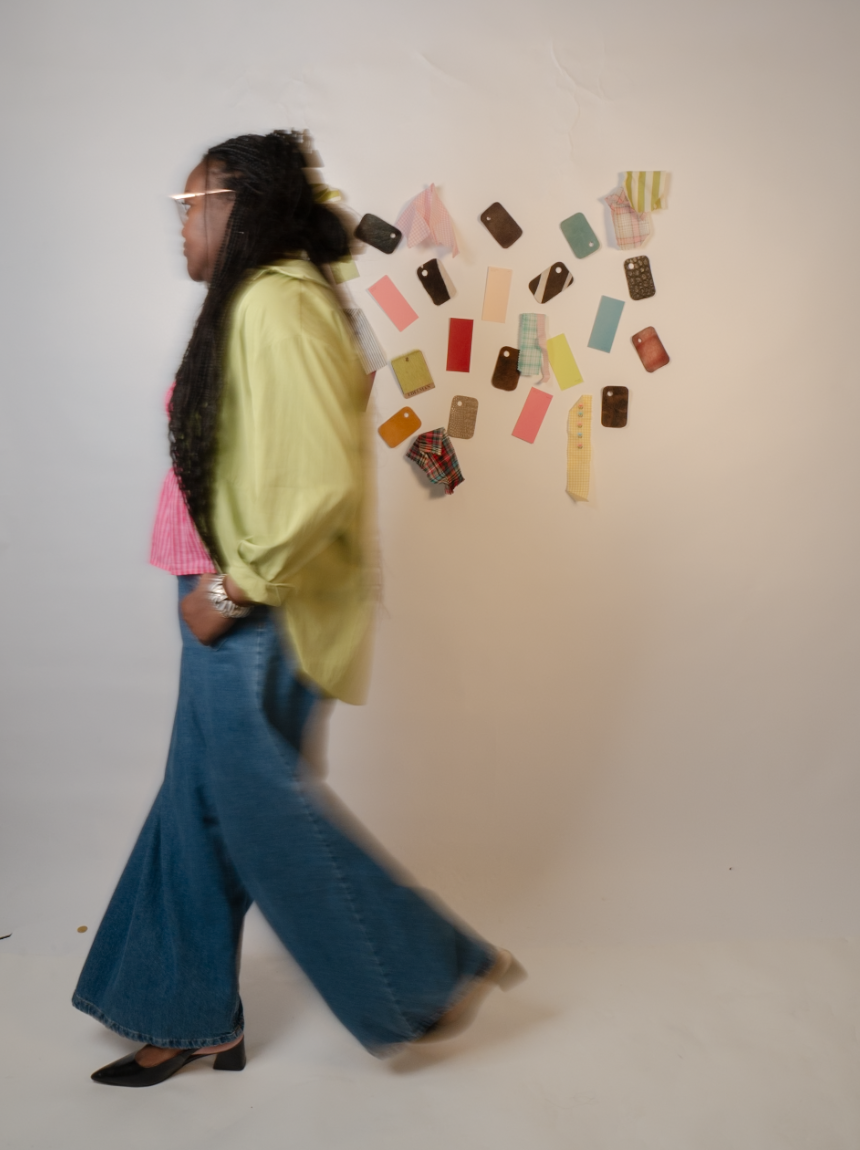 A woman walking past a plain wall decorated with various fabric swatches and color samples.