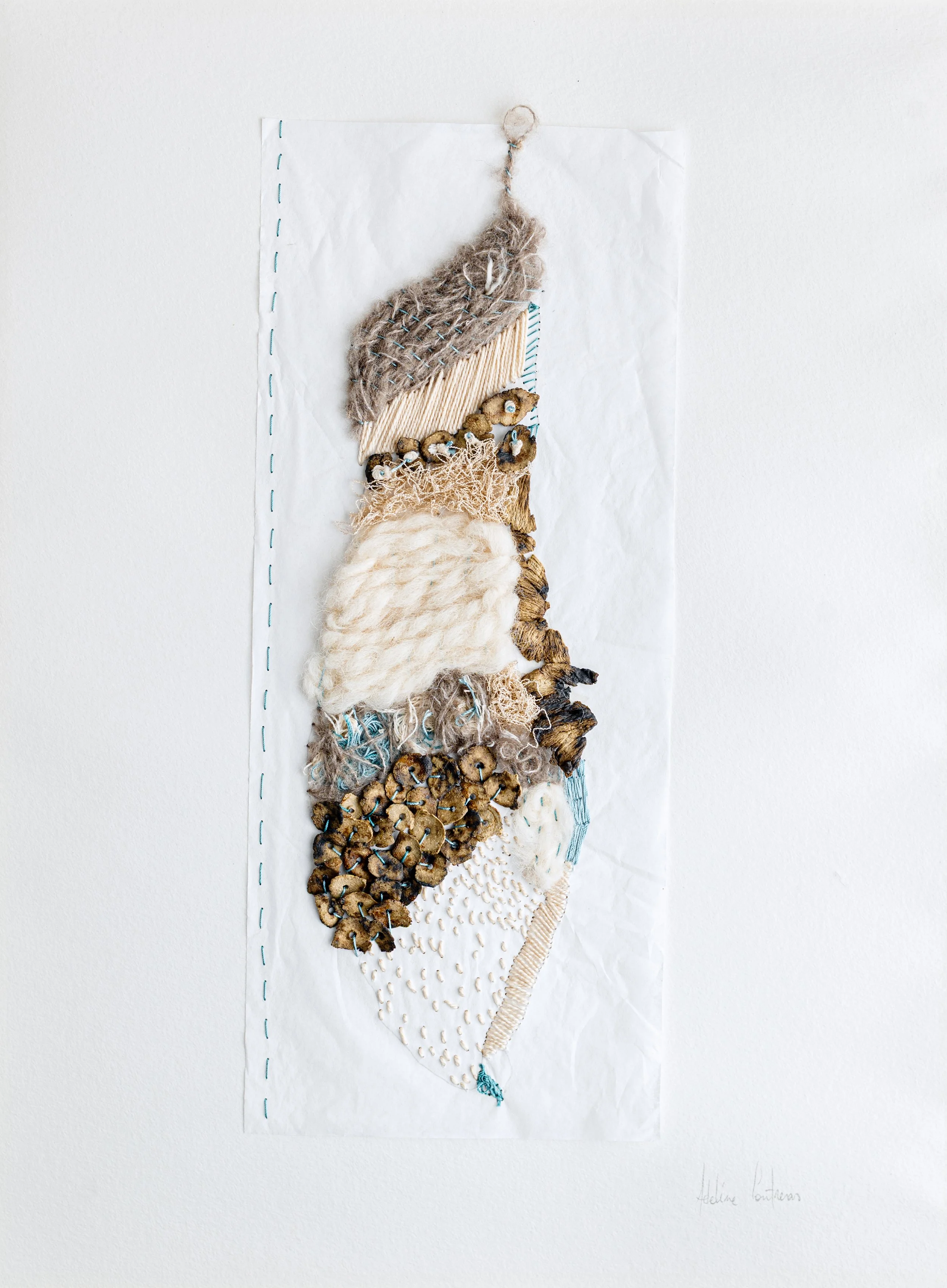 Une œuvre d'art composée de différents matériaux textiles, comme de la laine, des graines, des tissus, et du fil, assemblés pour créer une figure abstraite représentant une personne.