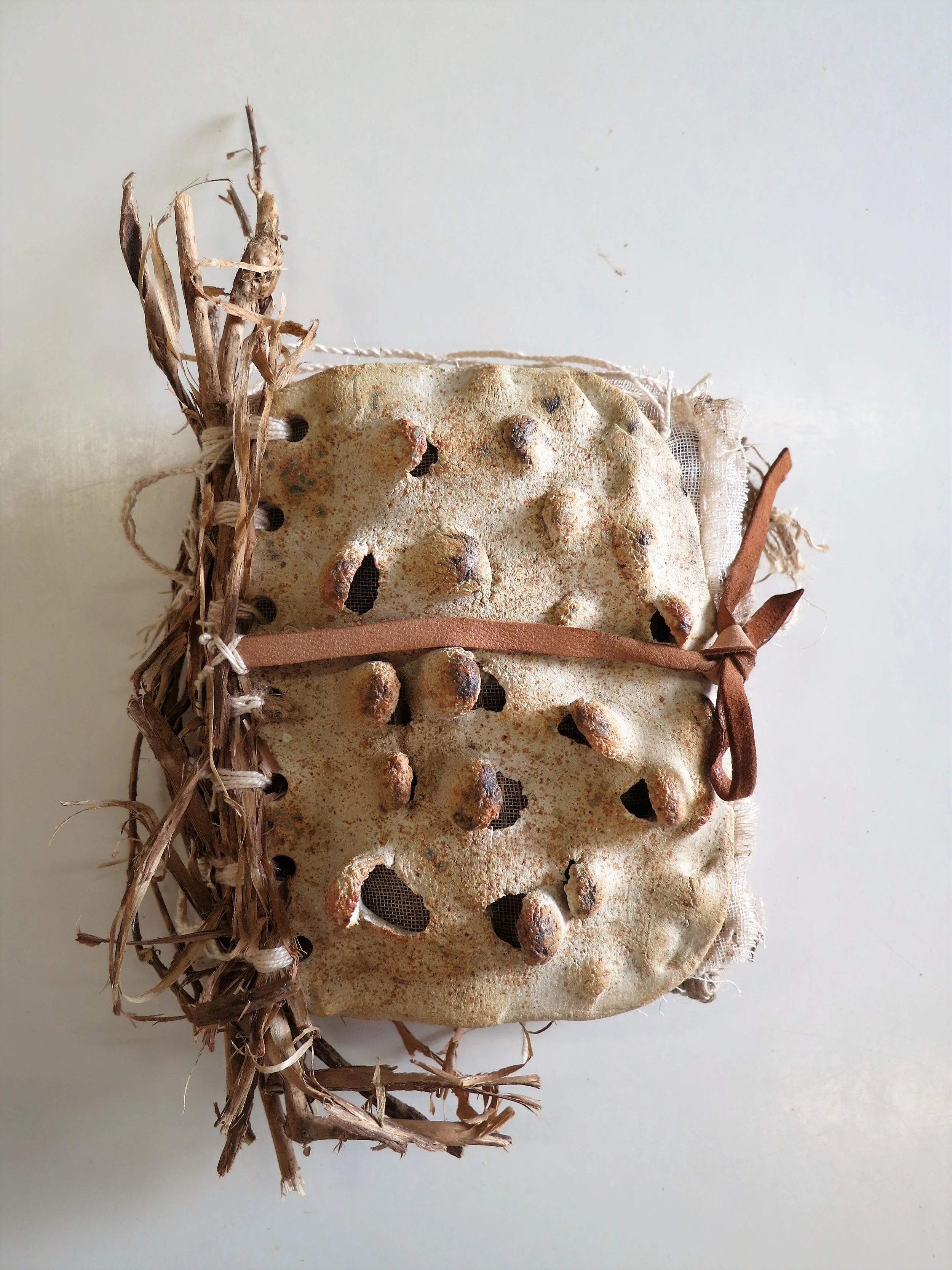 Une ancienne chaussure en toile, avec des trous, décorée de matériau naturel et de rubans en cuir, posée sur un fond blanc.