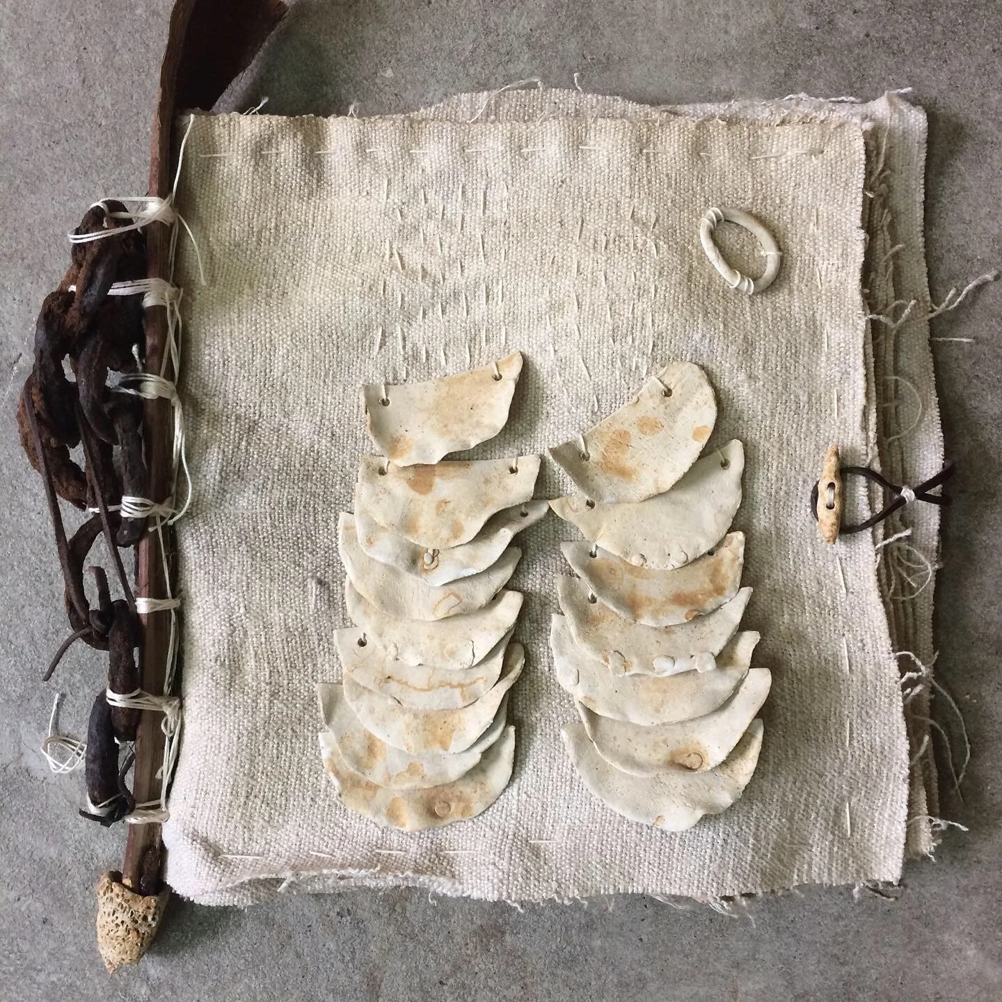 Fragment de coquillage posé sur un tissu beige, entouré d'une bordure fabriquée avec des branches et de la corde, pouvant être une œuvre artisanale ou une installation artistique.