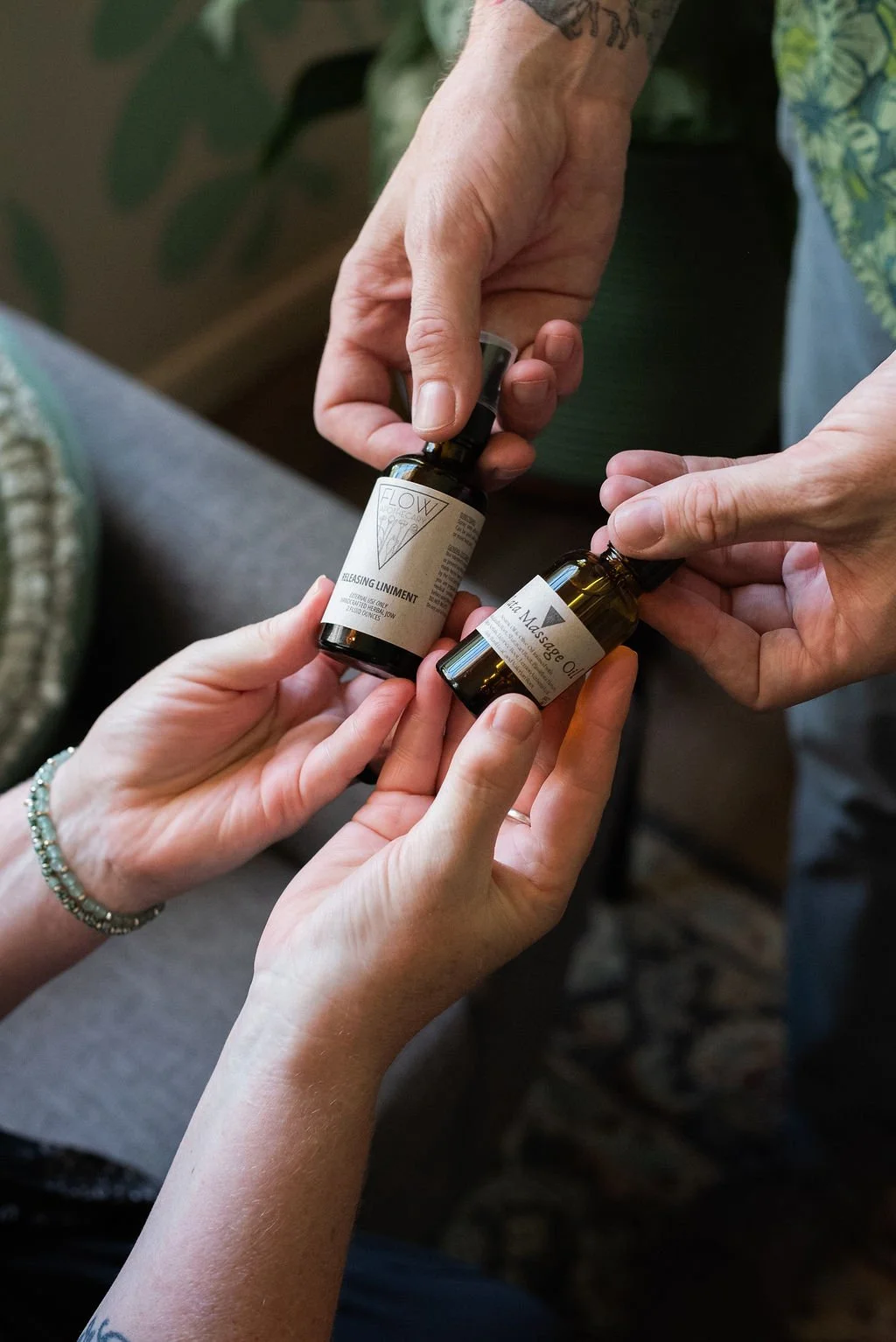Multiple hands holding small bottles of massage oil, labeled 'Flow' and 'Unblocking Uninment'.