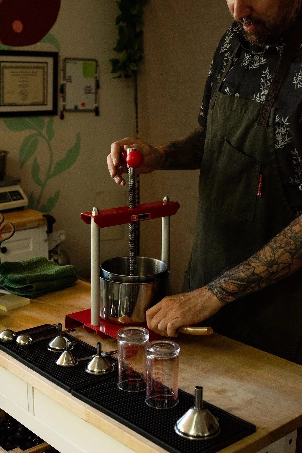 A person with tattoos on their arm using a manual popcorn maker at a countertop.