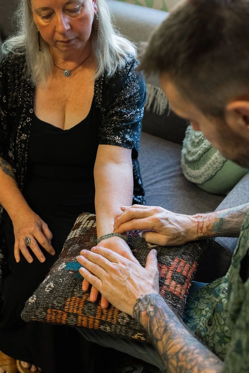 A woman with long gray hair listening as a man tattoos her arm.