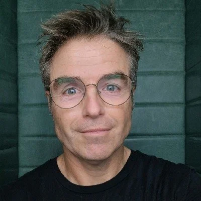 Persona con gafas y camiseta negra, fondo acolchado verde.