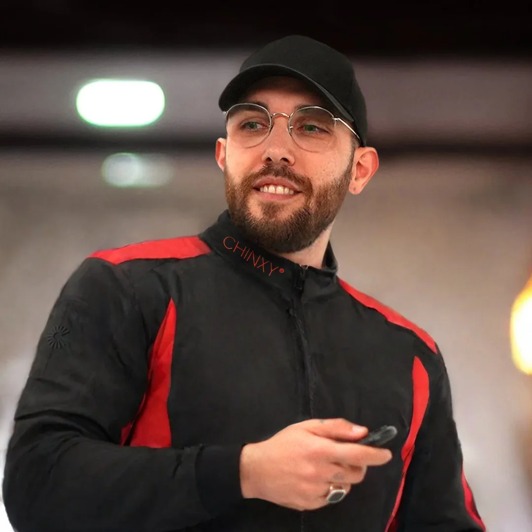 Hombre con barba y gafas, vistiendo chaqueta negra y roja, y gorra negra.