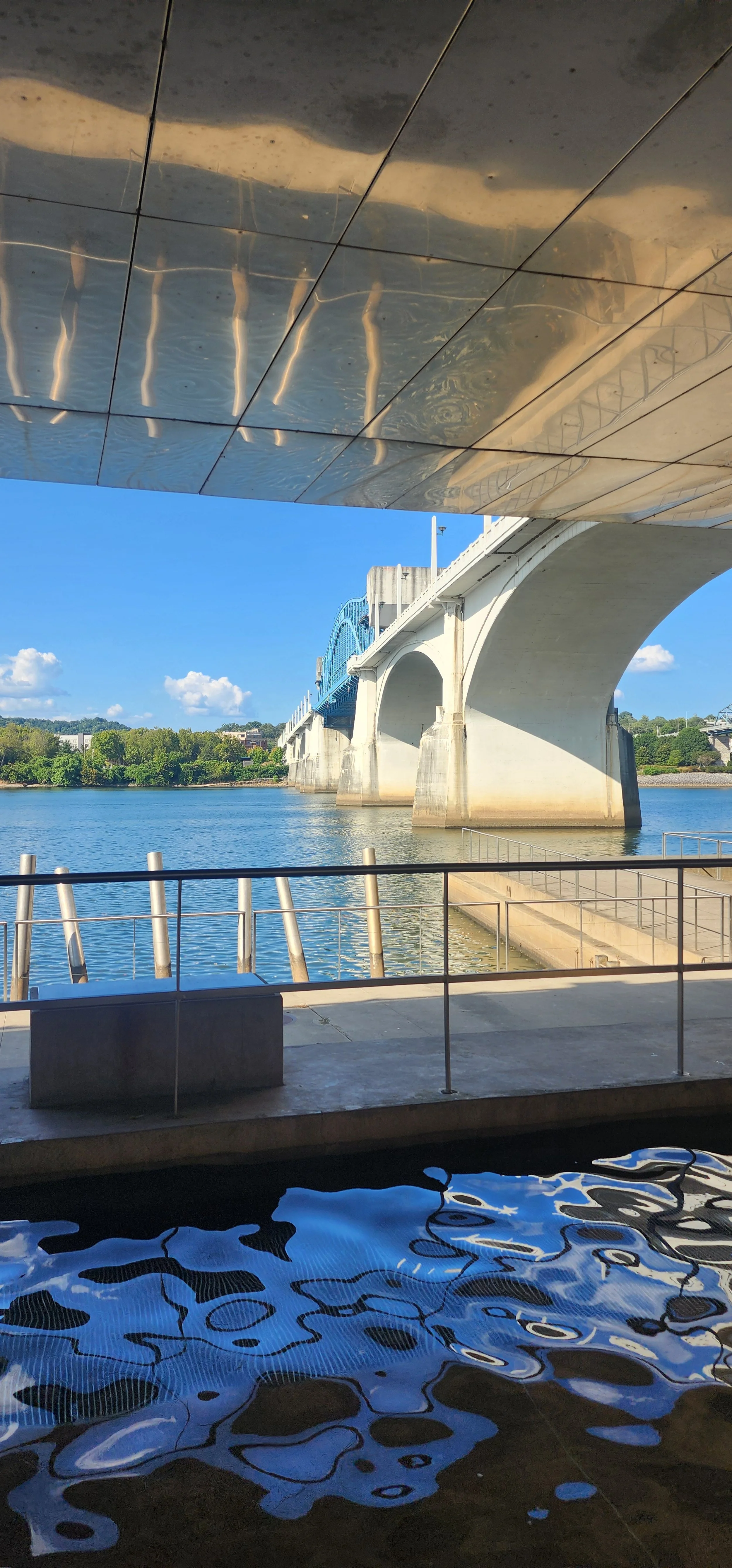 Bridge over a river with a reflection on a wavy water surface, viewed from underneath a ceiling with reflections of the water.