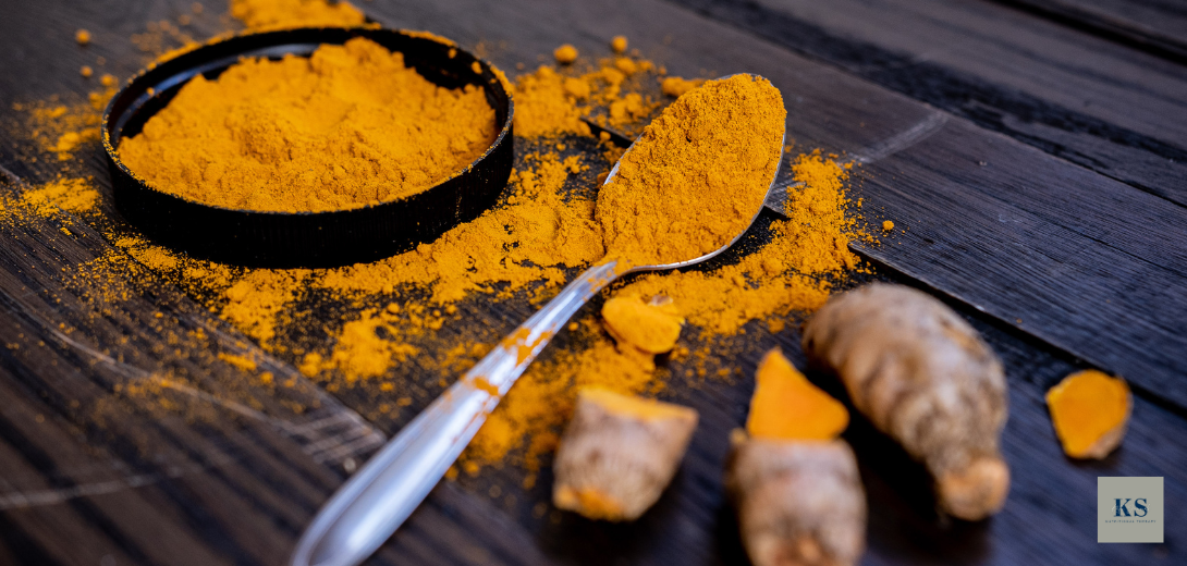ground turmeric powder on spoon with turmeric root